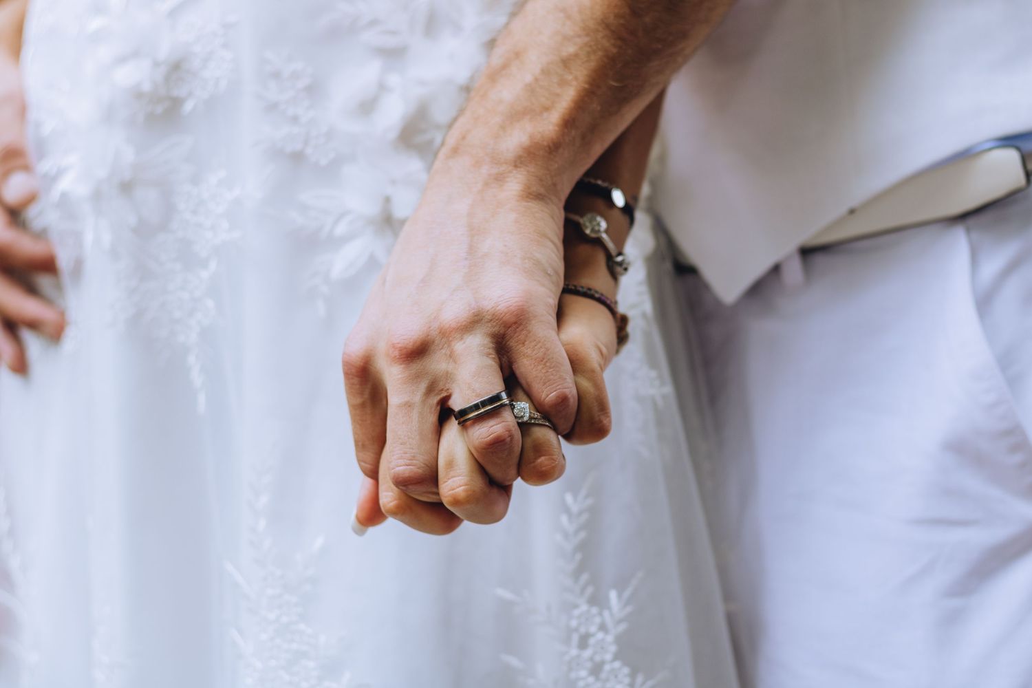 A bridal jewelry collection showing hands with rings, pearls, and delicate bridal accessories against a white lace background.