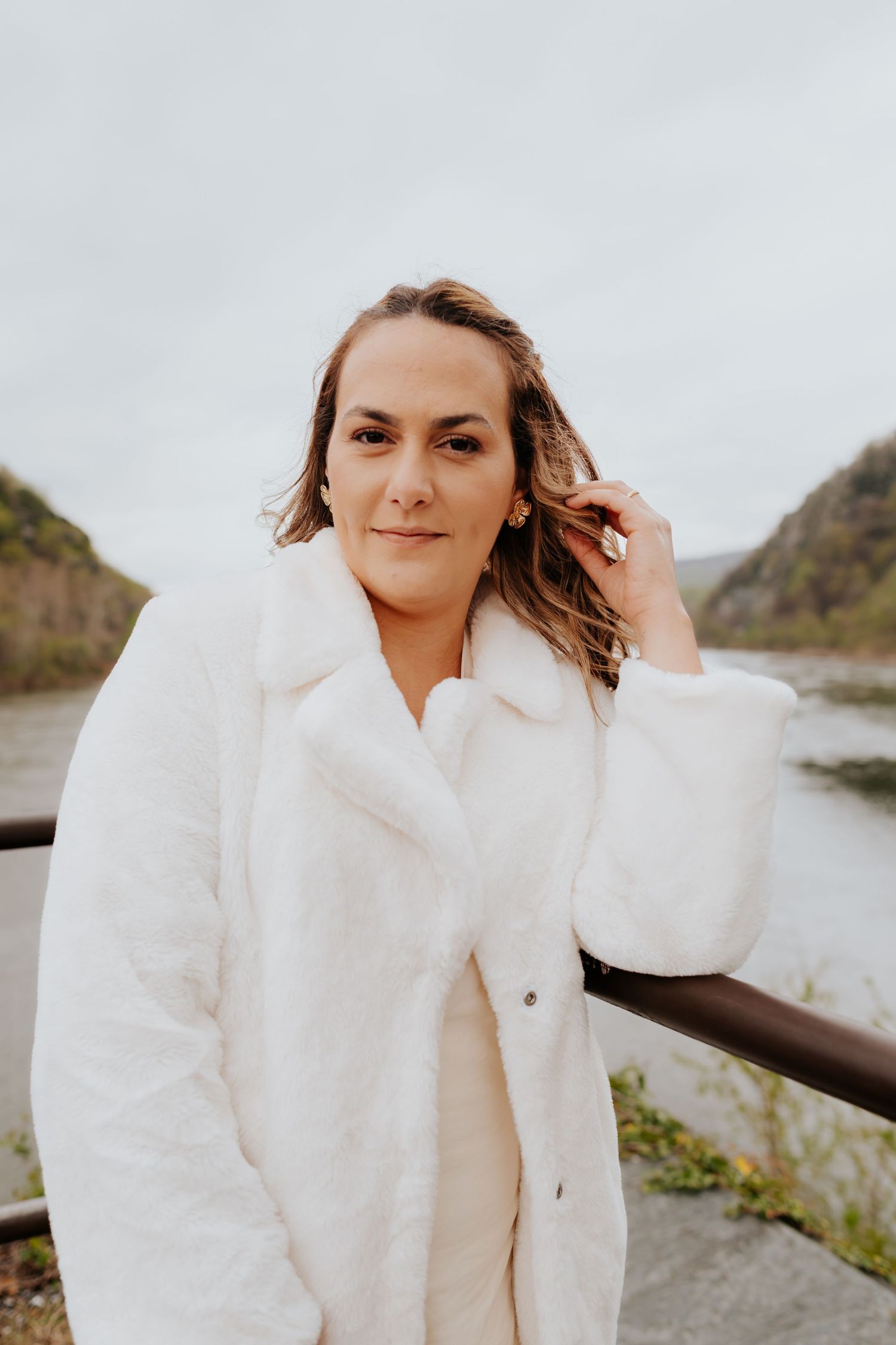 Progression of shots showing someone in a cozy white fur coat posing by water.