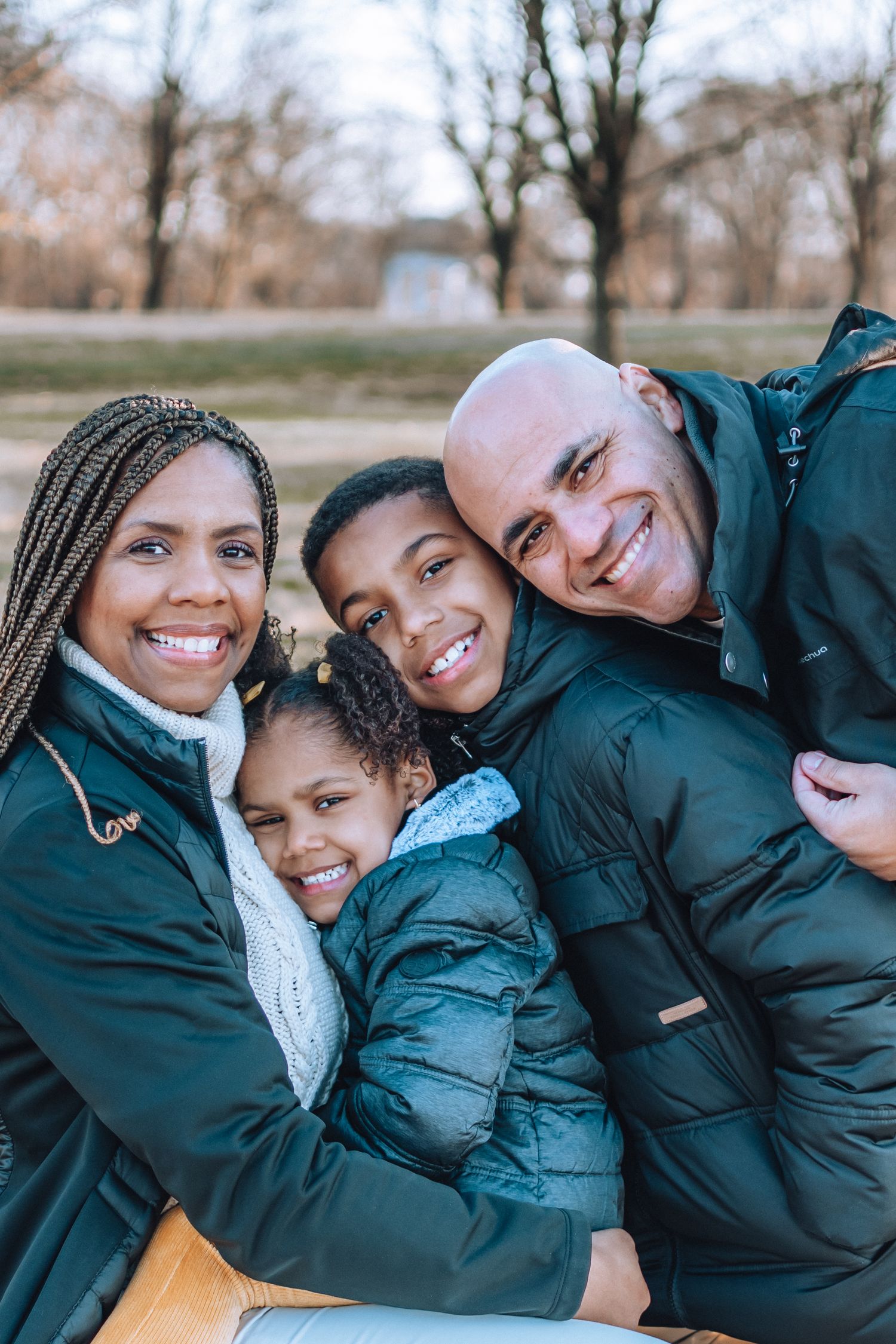 A family wearing matching green winter coats huddles together outdoors on a cool autumn day.