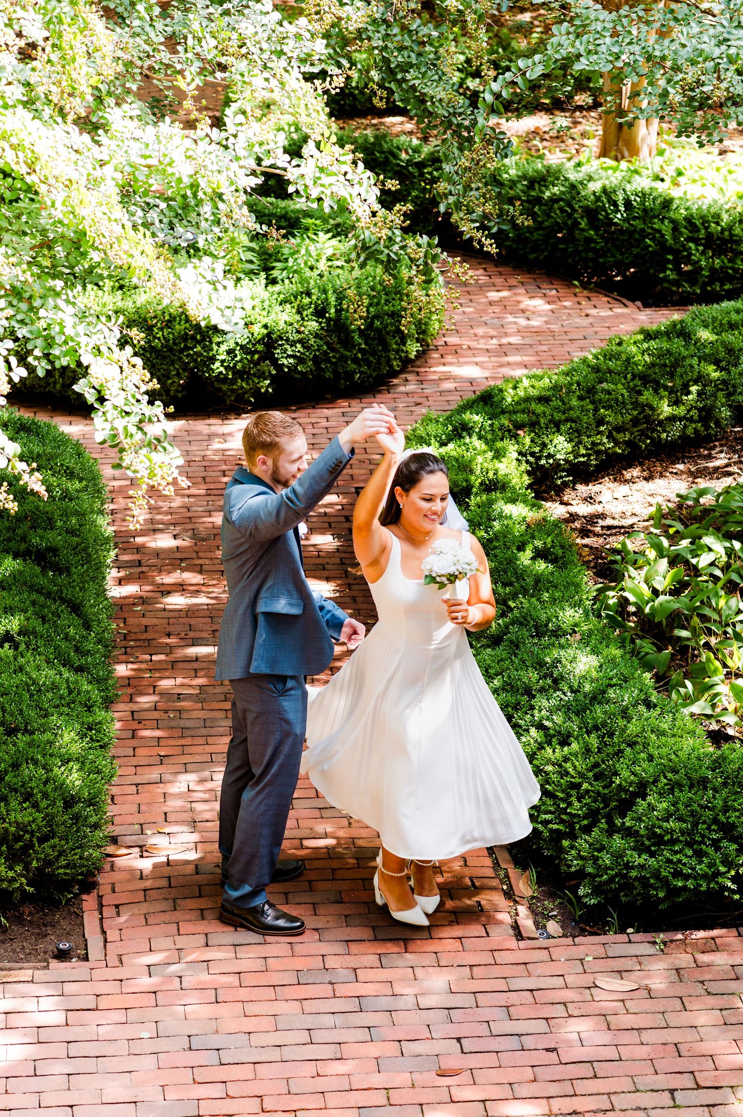Dancing newlyweds on a brick pathway surrounded by lush garden greenery.