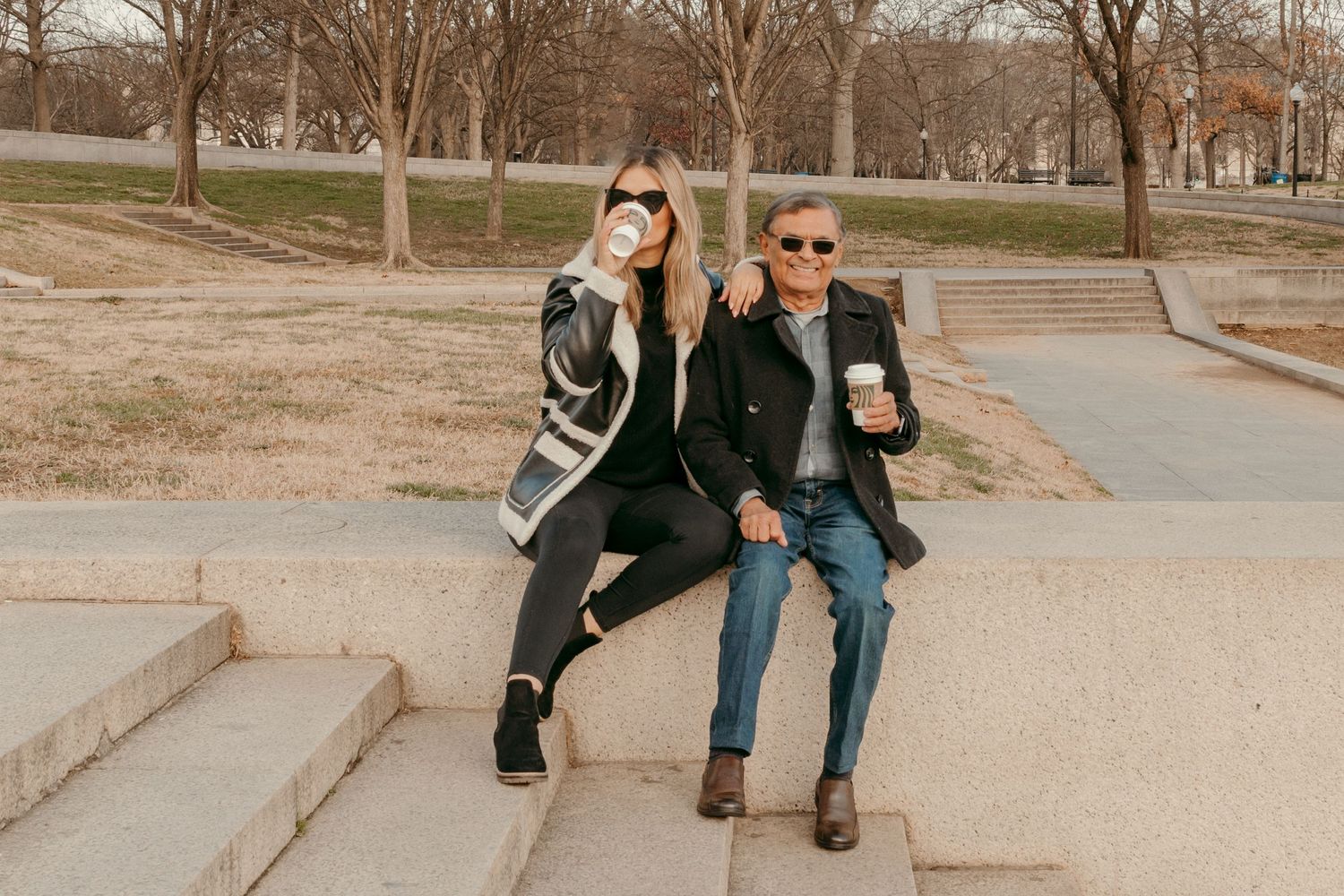 Two people in sunglasses sitting together on concrete steps outdoors.