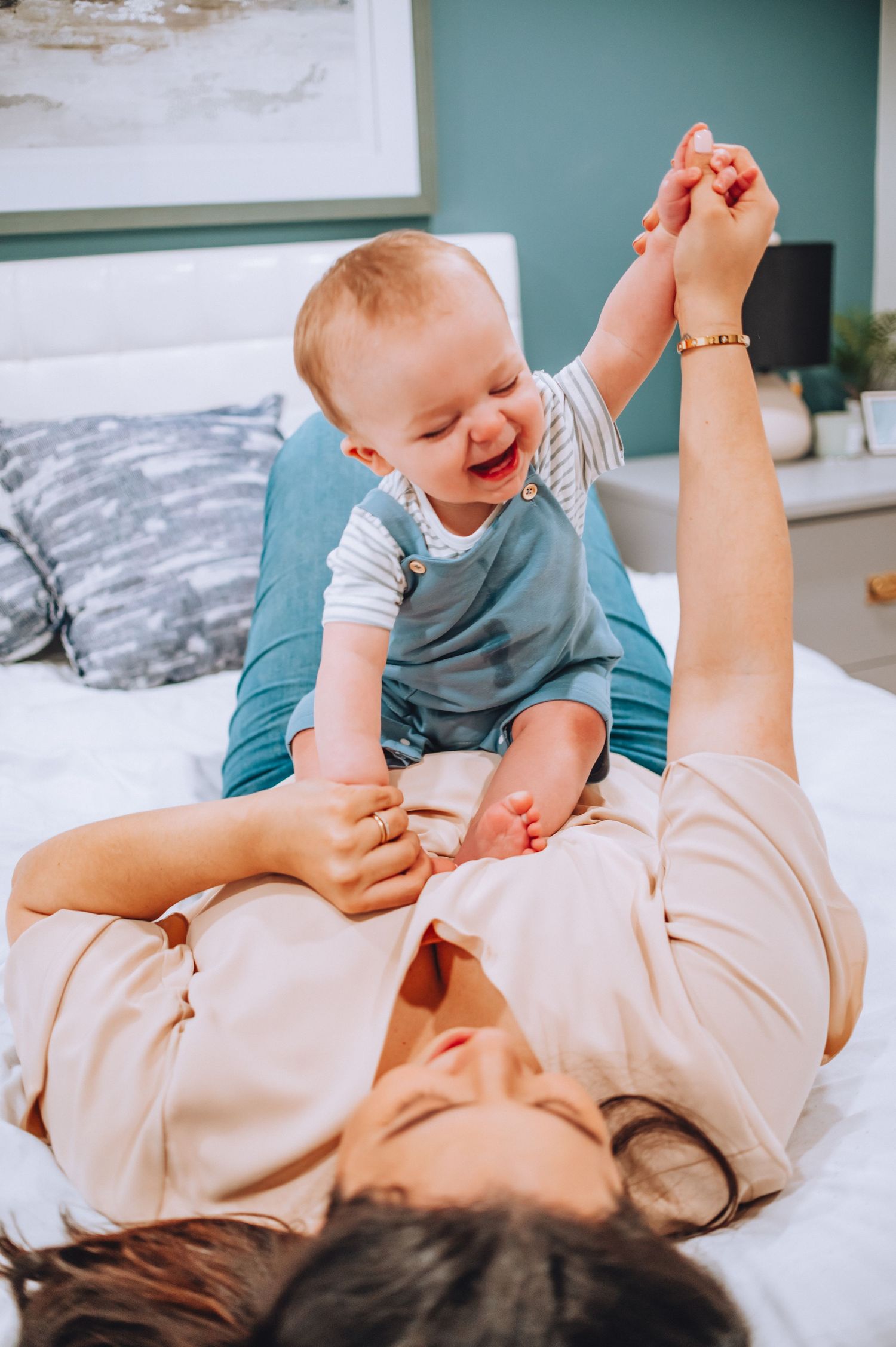 Parent and baby share a joyful moment while playing together on white bedding.