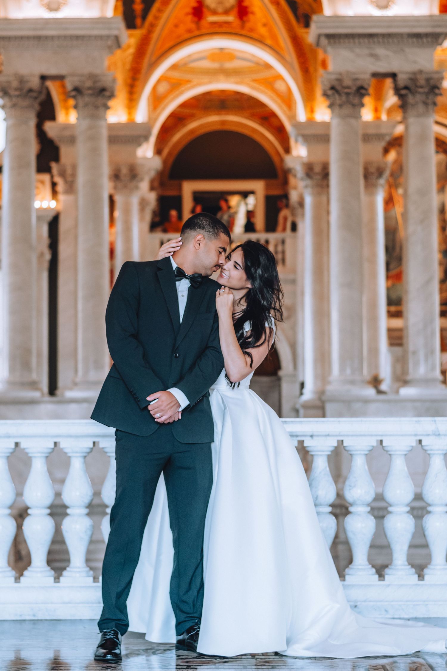 A romantic wedding couple embraces against a backdrop of elegant marble columns and arches at sunset.