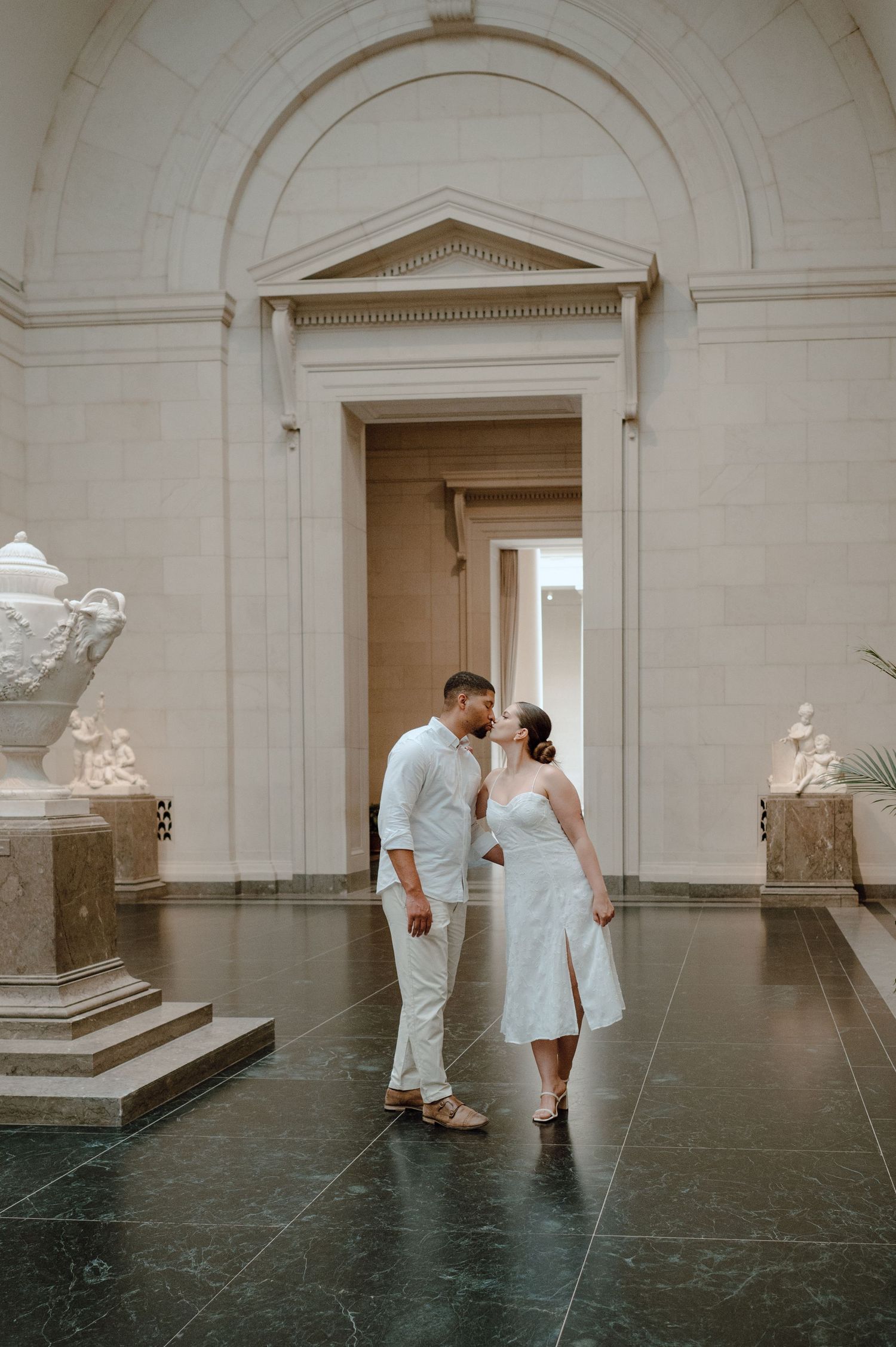 Romantic moment captured in a museum hallway with neoclassical architecture and decorative urns.