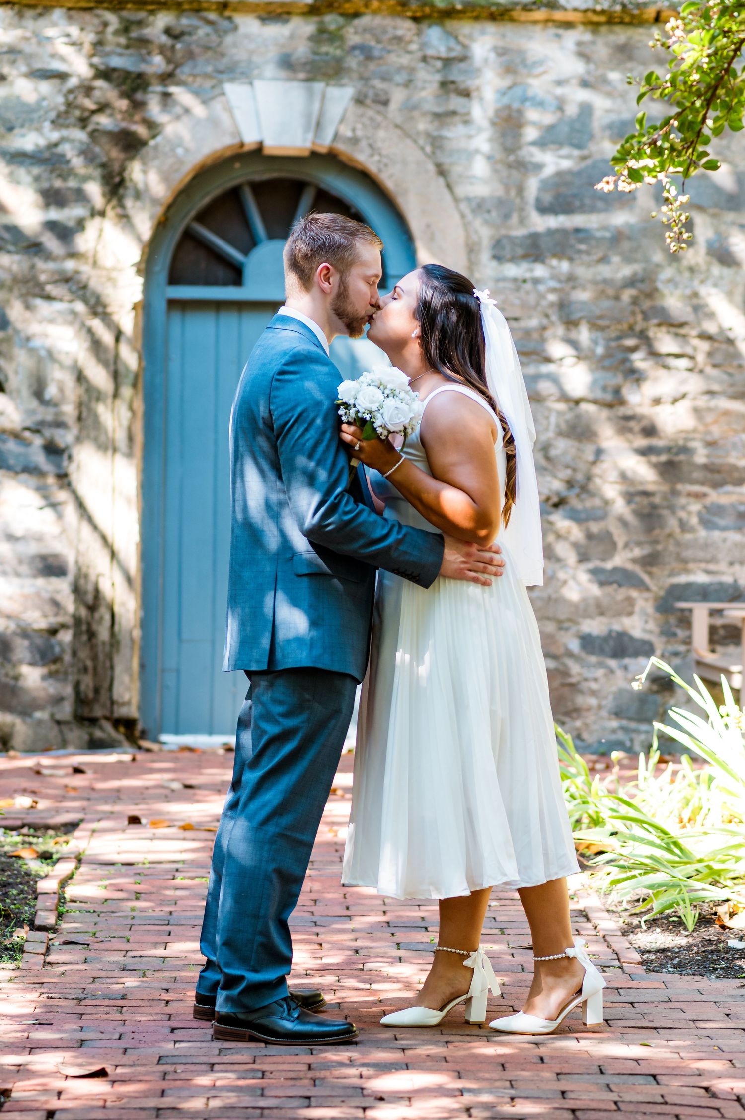 Romantic moment between newlyweds standing on brick pavement in front of historic stone building.
