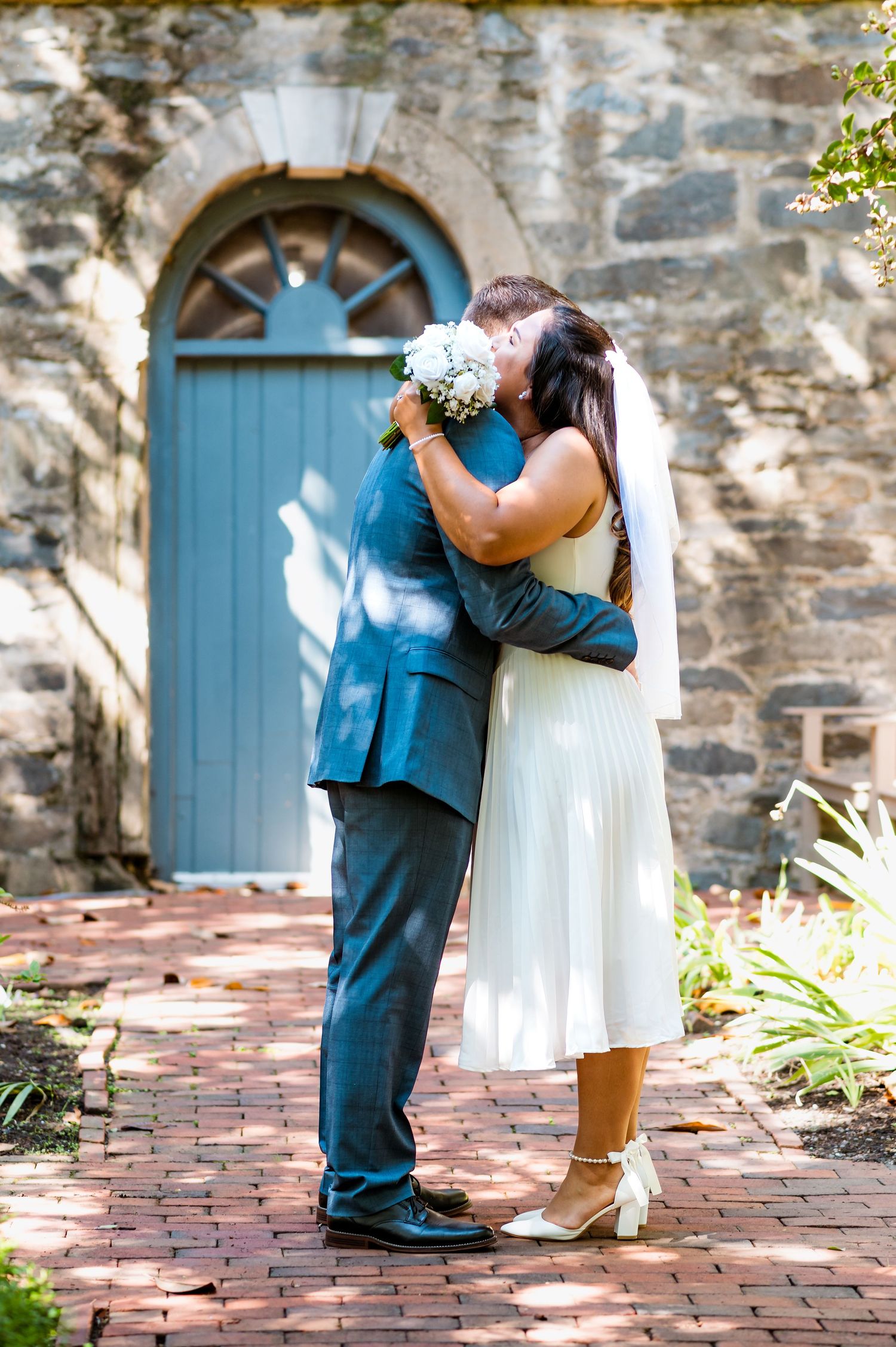 Four sequential photos show a romantic moment between a couple on a brick pathway with rustic stone walls and blue doors.