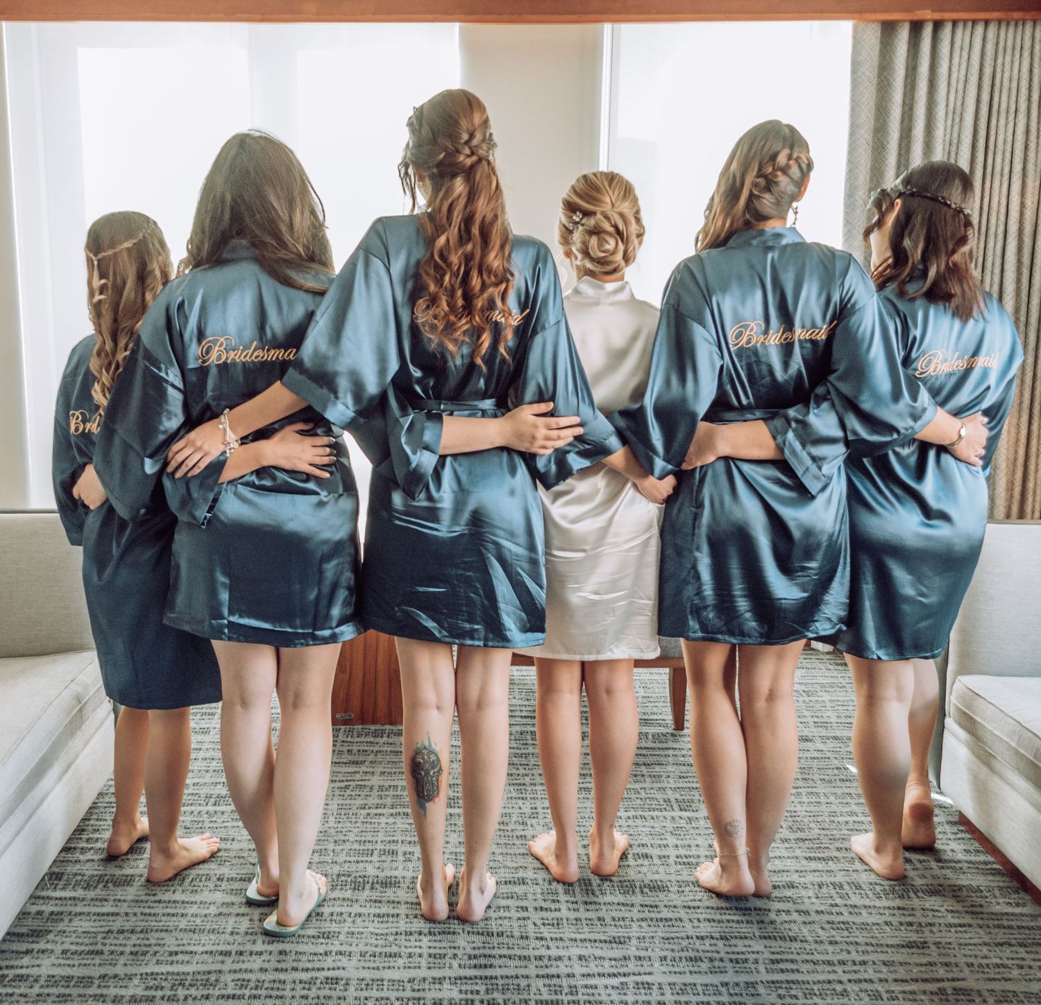 Bridesmaids in matching blue silk robes pose with their backs to the camera.