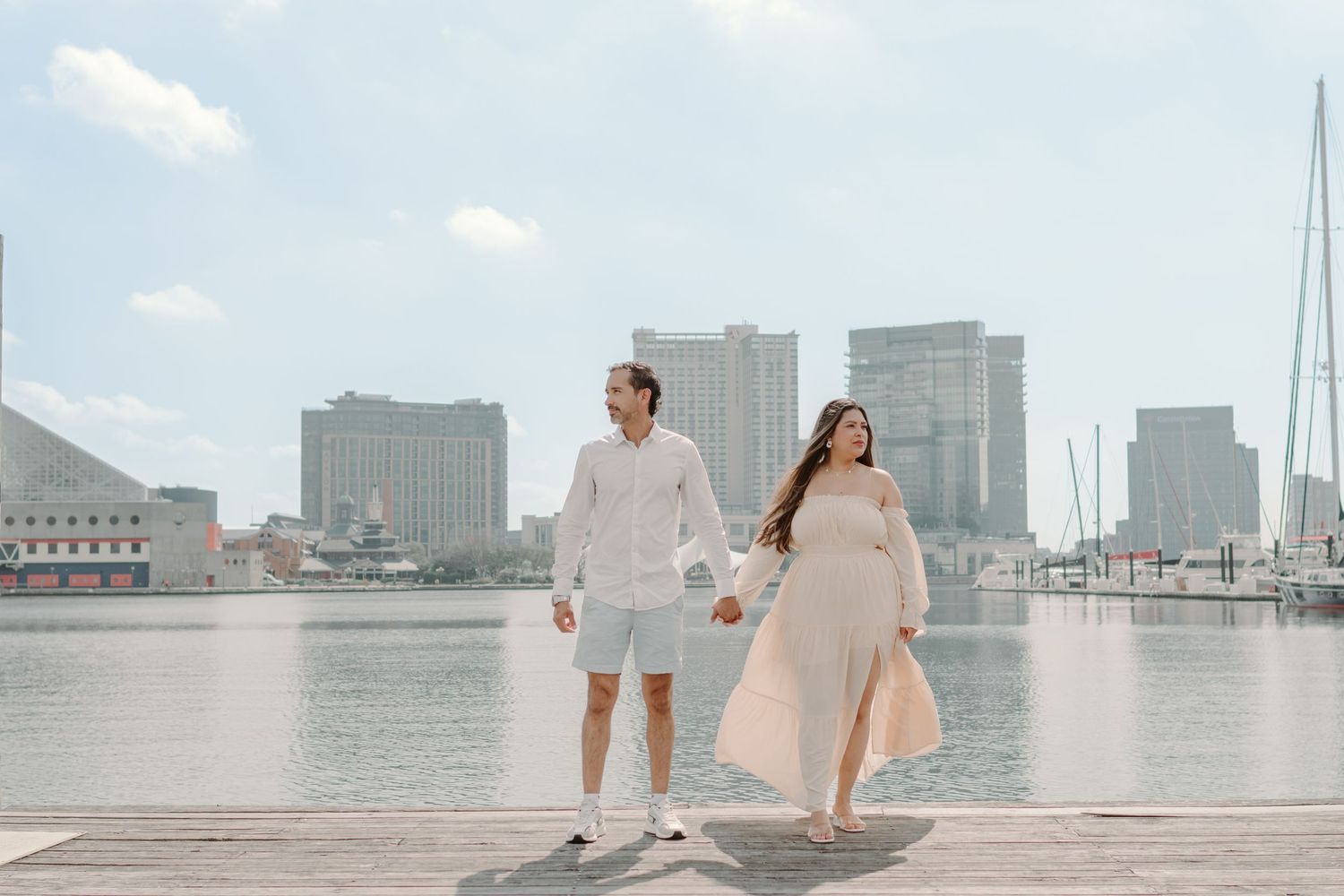 A couple poses together at a waterfront marina with the city skyline and boats in the background.