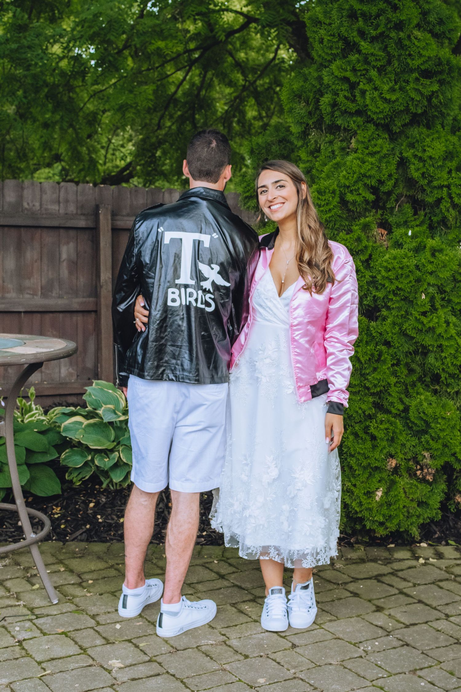 1950s style couple in matching jackets with contrasting white tulle skirt and shorts pose in garden setting by fence.