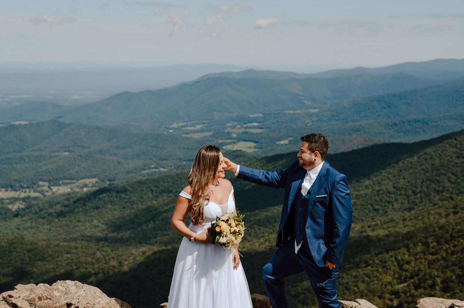 A couple shares romantic moments against a scenic mountain backdrop during their wedding photoshoot.