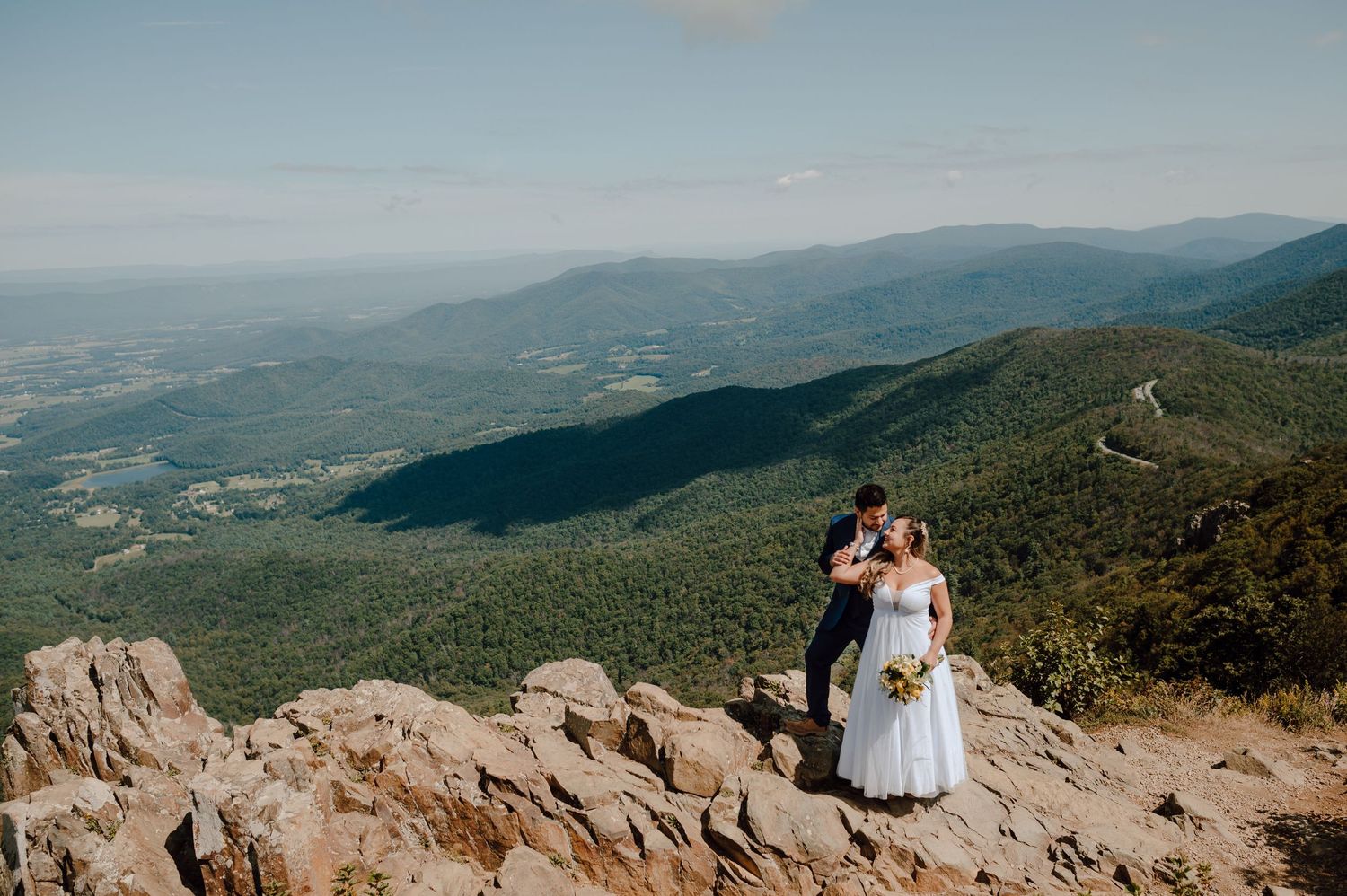 A couple poses for wedding photos with sweeping mountain vistas and lush green valleys in the background.
