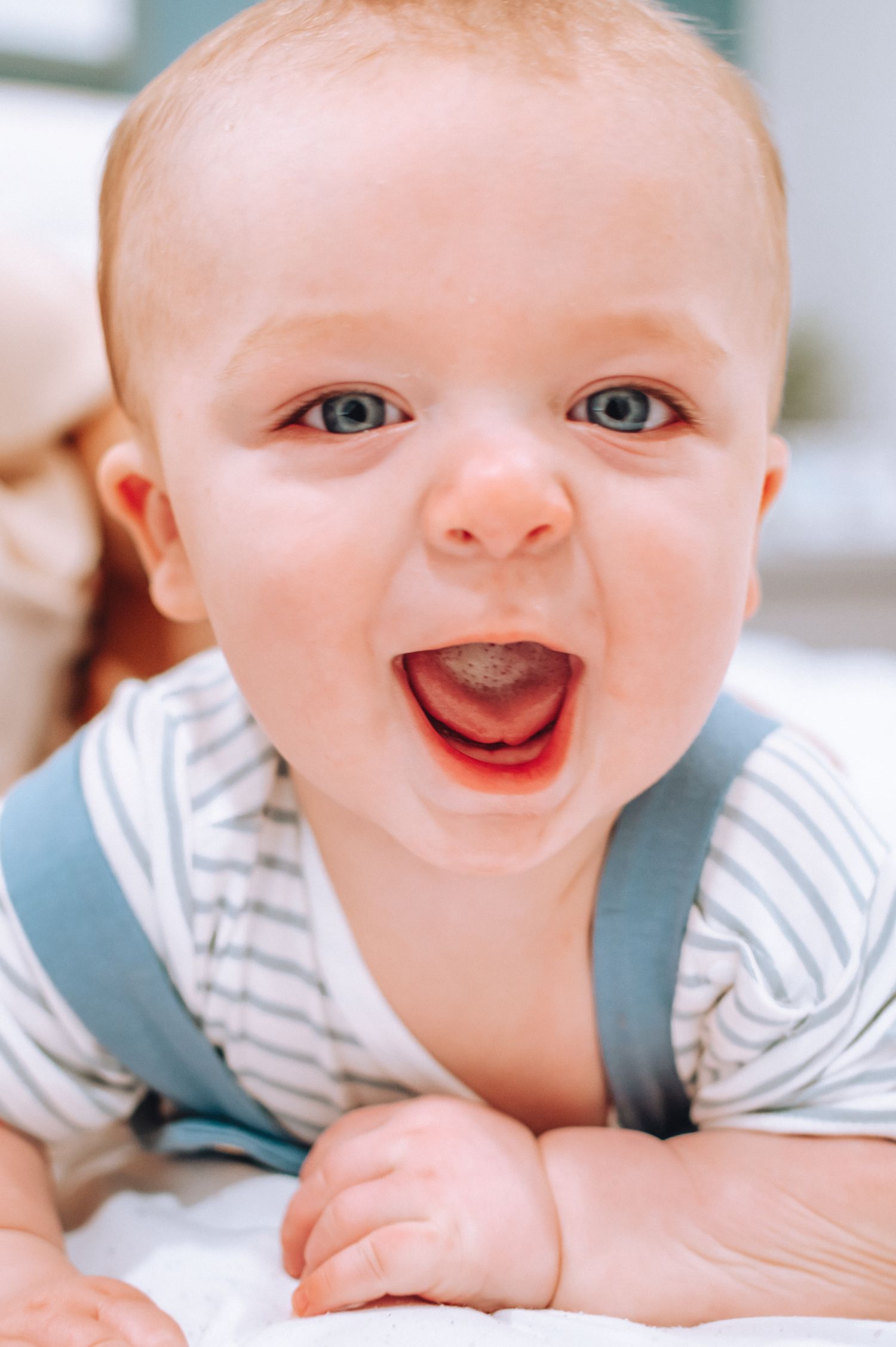 Closeup of a happy baby in striped shirt and blue overalls showing a bright smile.