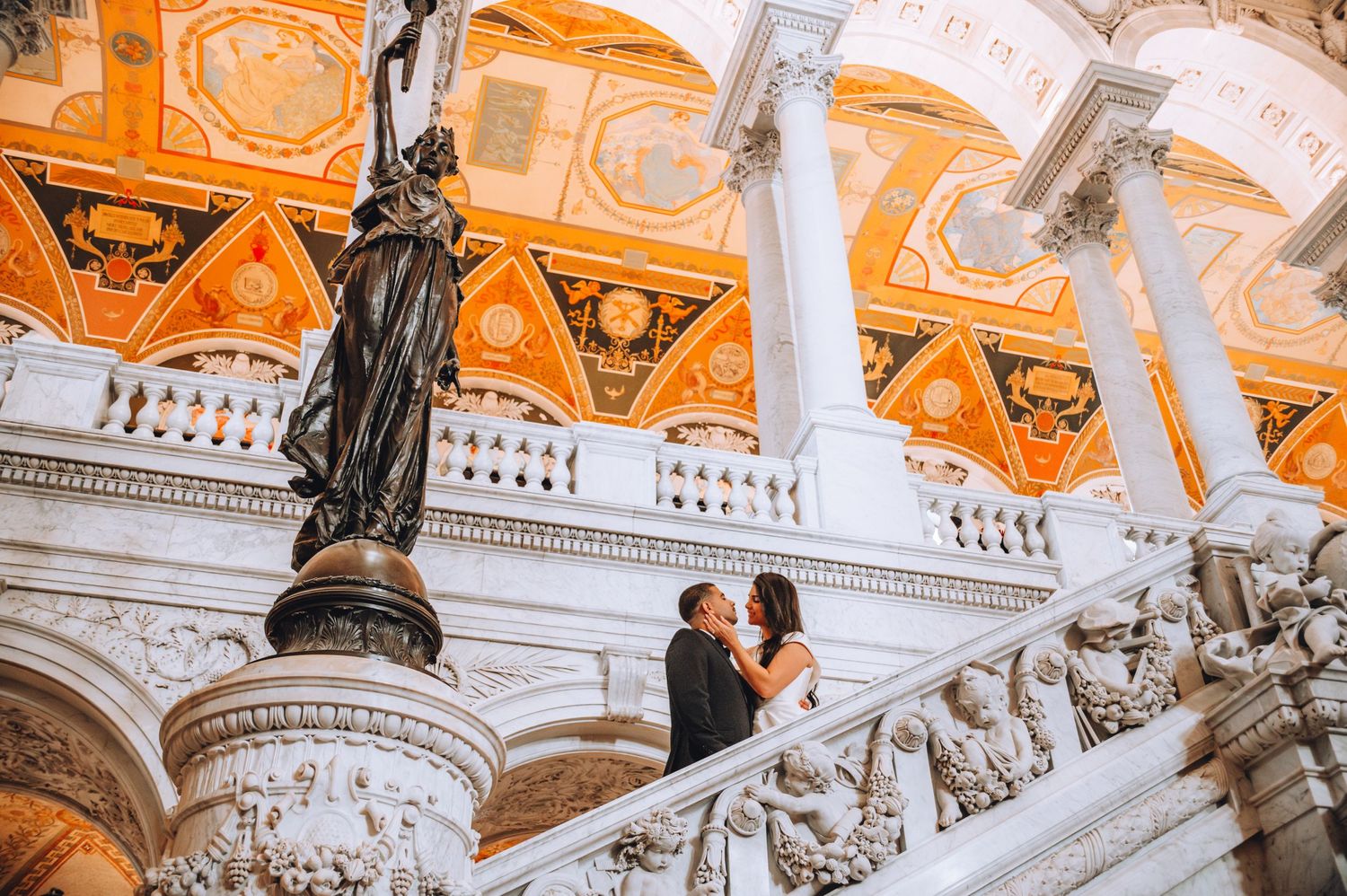 A couple stands on the ornate marble staircase inside the Library of Congress with its grand classical architecture.