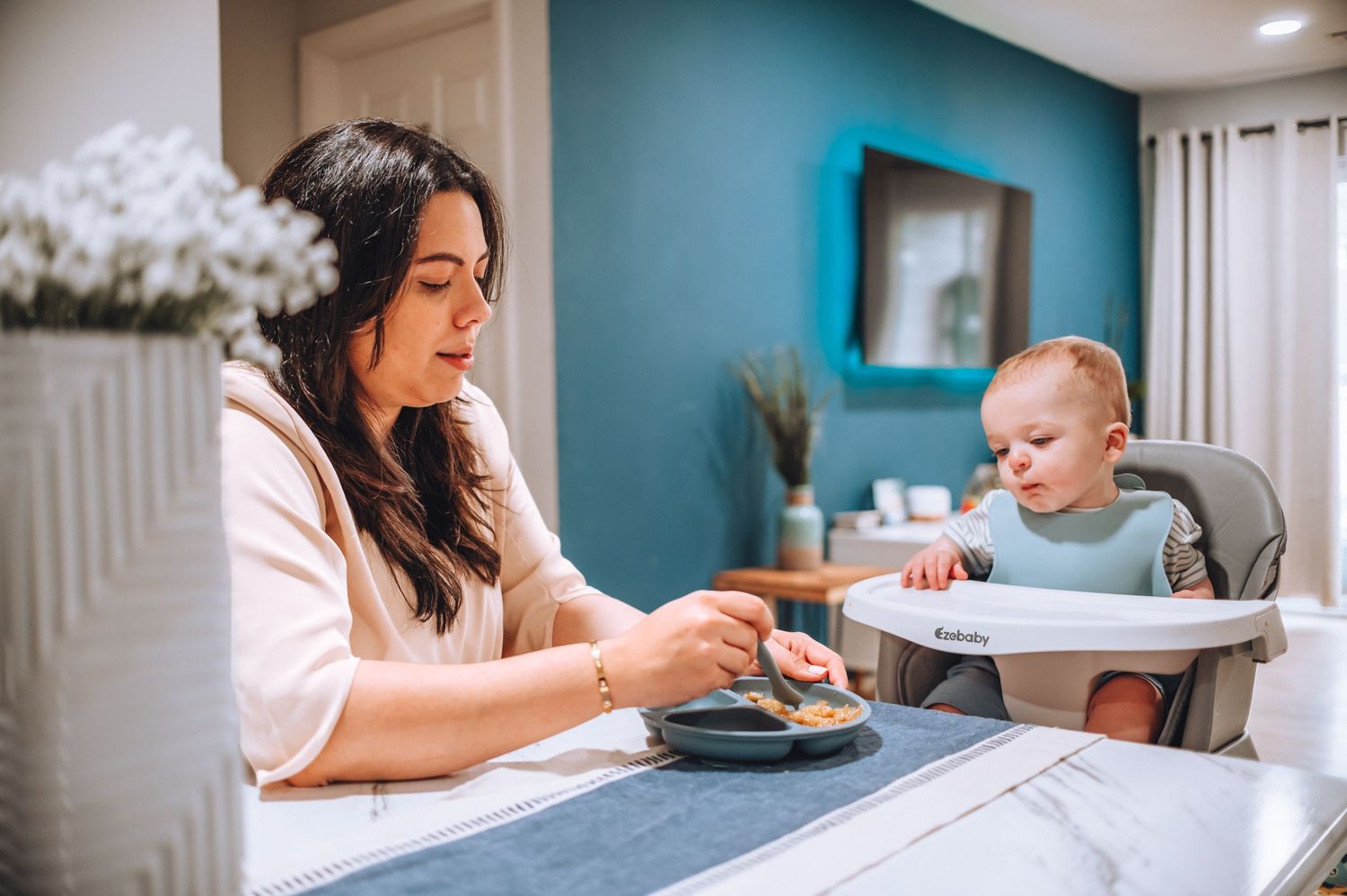 Parent and baby sharing mealtime moment at dining table.