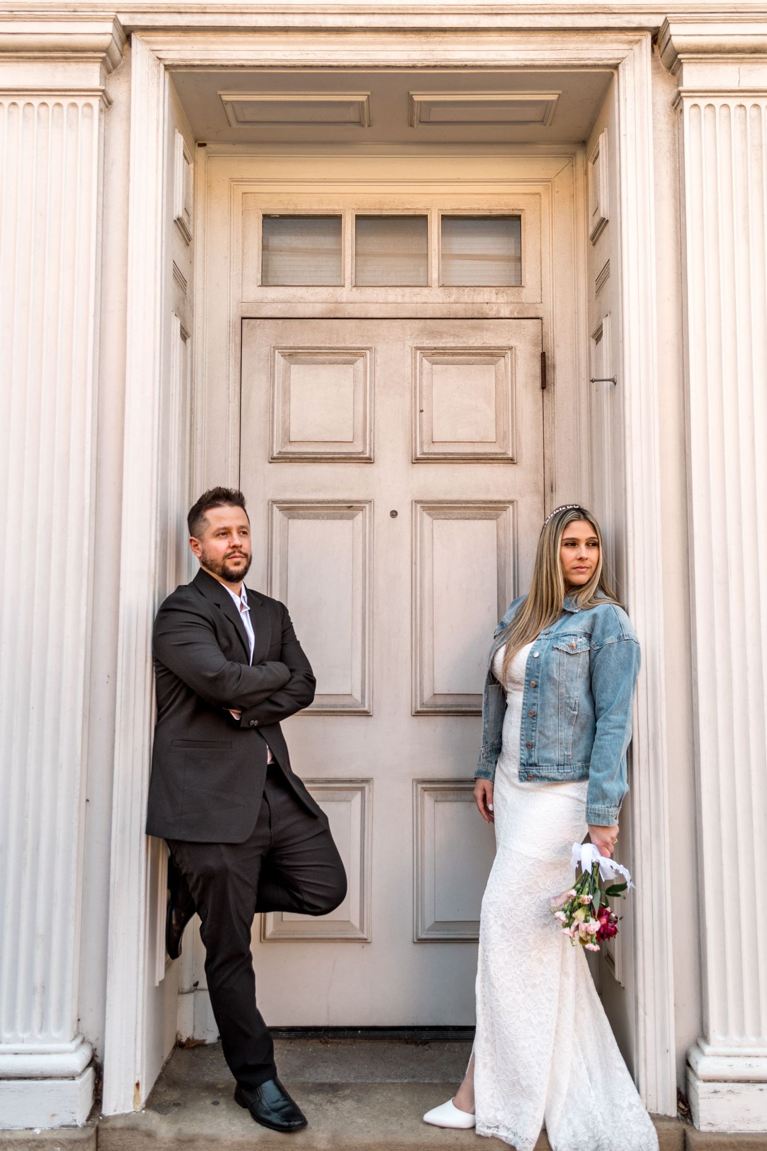 Stylish wedding portrait of couple standing in front of classic white columned doorway.