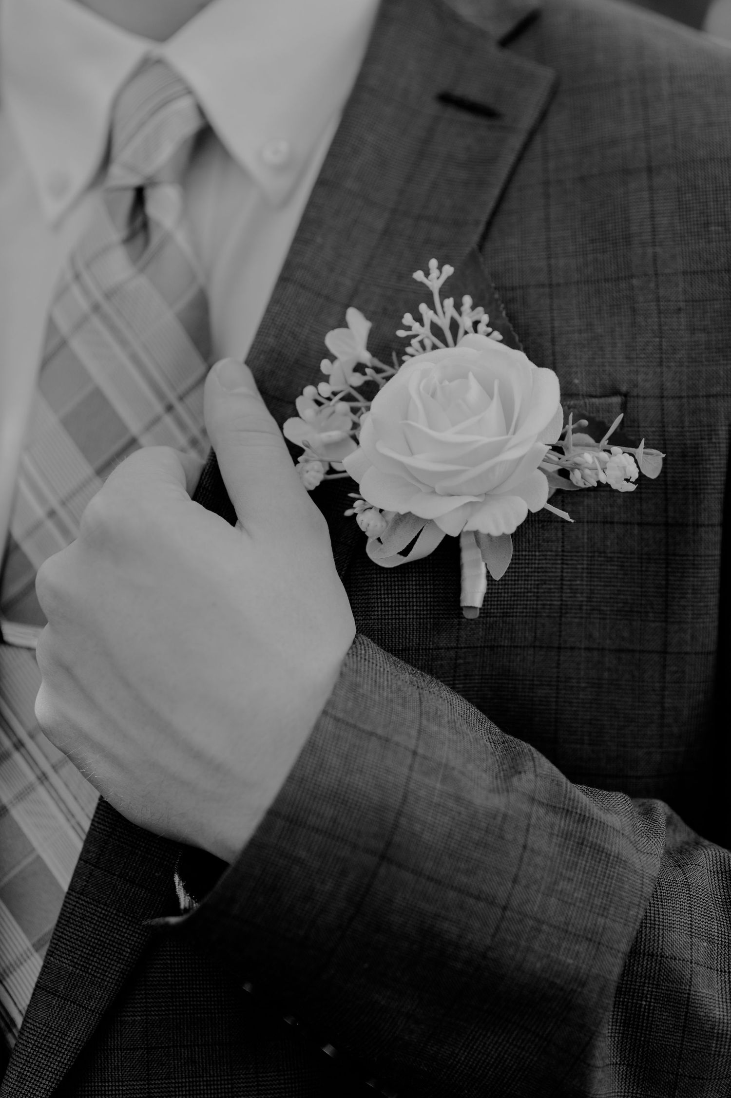 Close-up of white rose boutonniere on gray suit jacket.