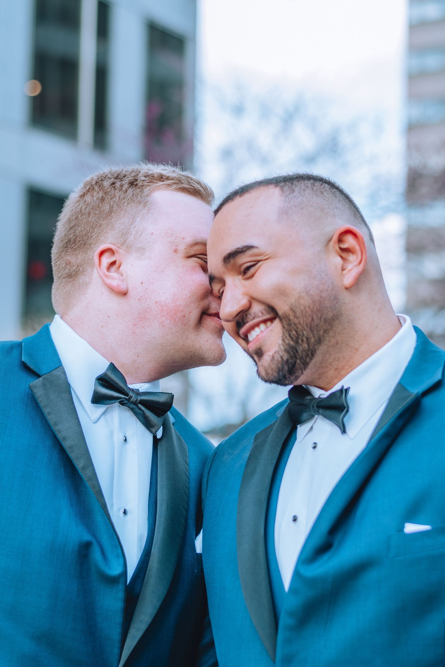 A sweet moment between two grooms in formal tuxedos sharing an intimate kiss during their wedding celebration.