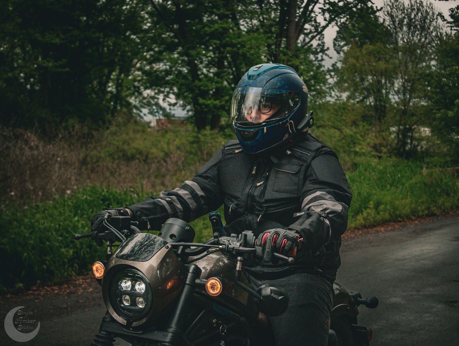 A black motorcycle cruises down a winding forest road in various dynamic shots.