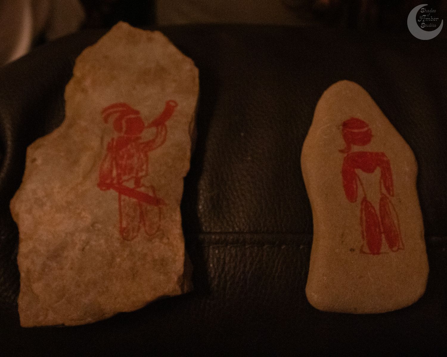 Two pieces of stone or clay with primitive red figures drawn on them against a dark leather background.