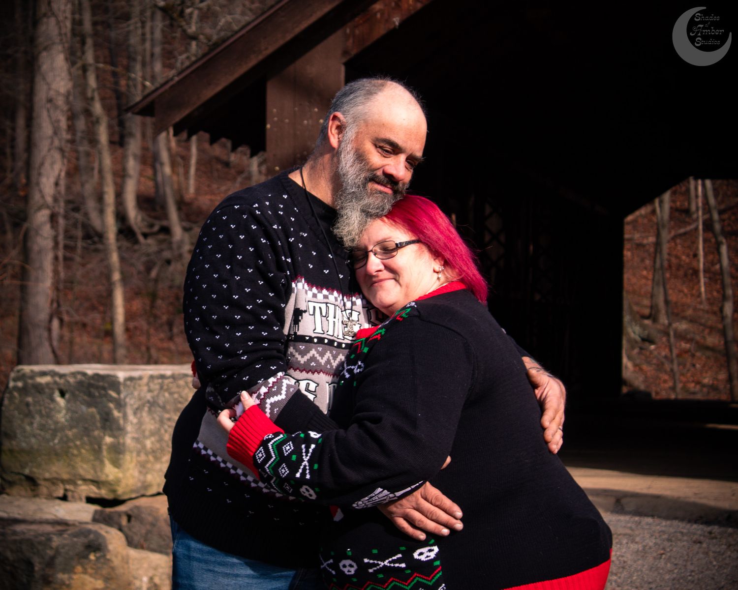 A couple in winter sweaters share a tender embrace while standing on a rustic wooden porch.