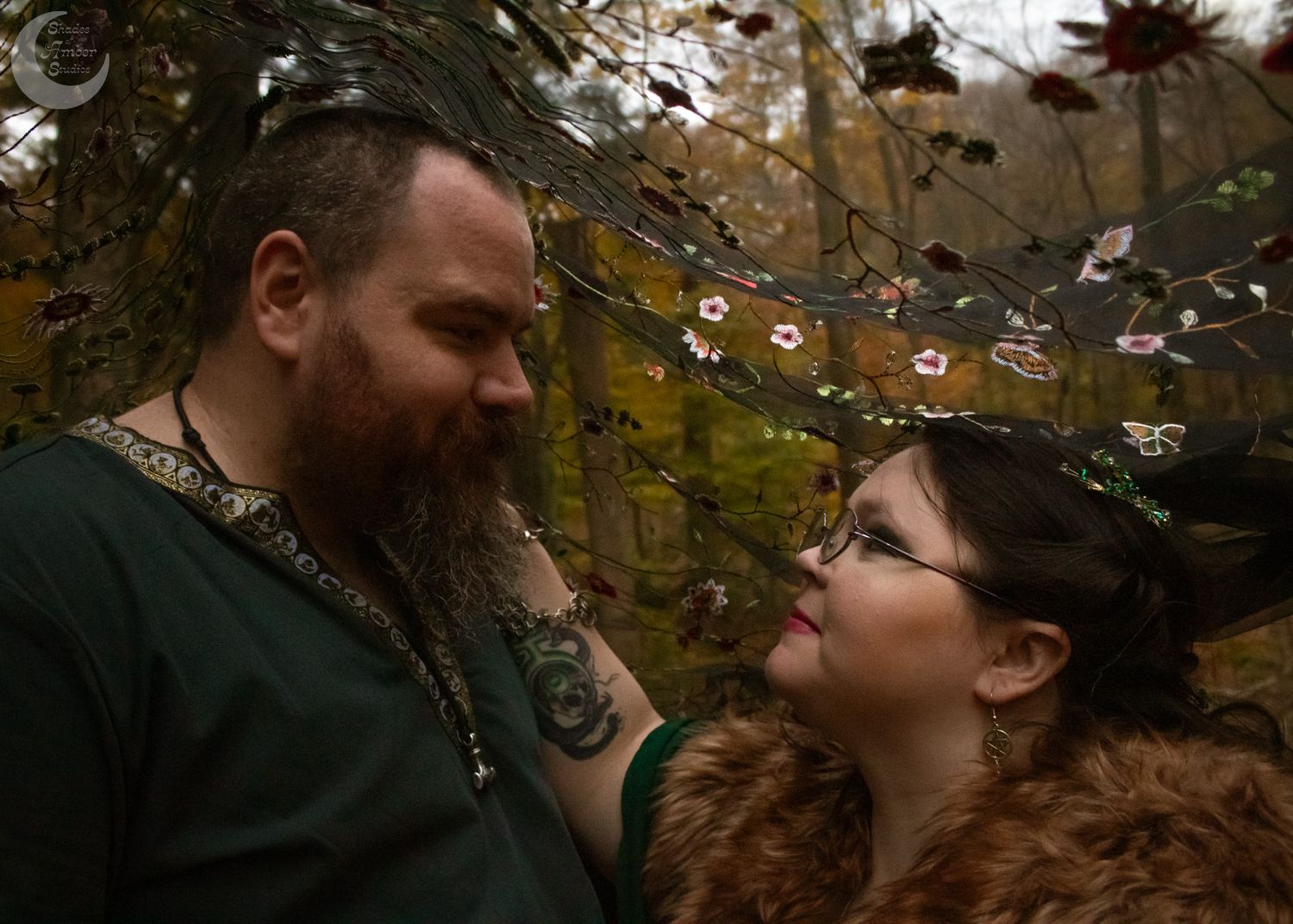 A couple shares an intimate moment together while standing outdoors among autumn trees and falling leaves.