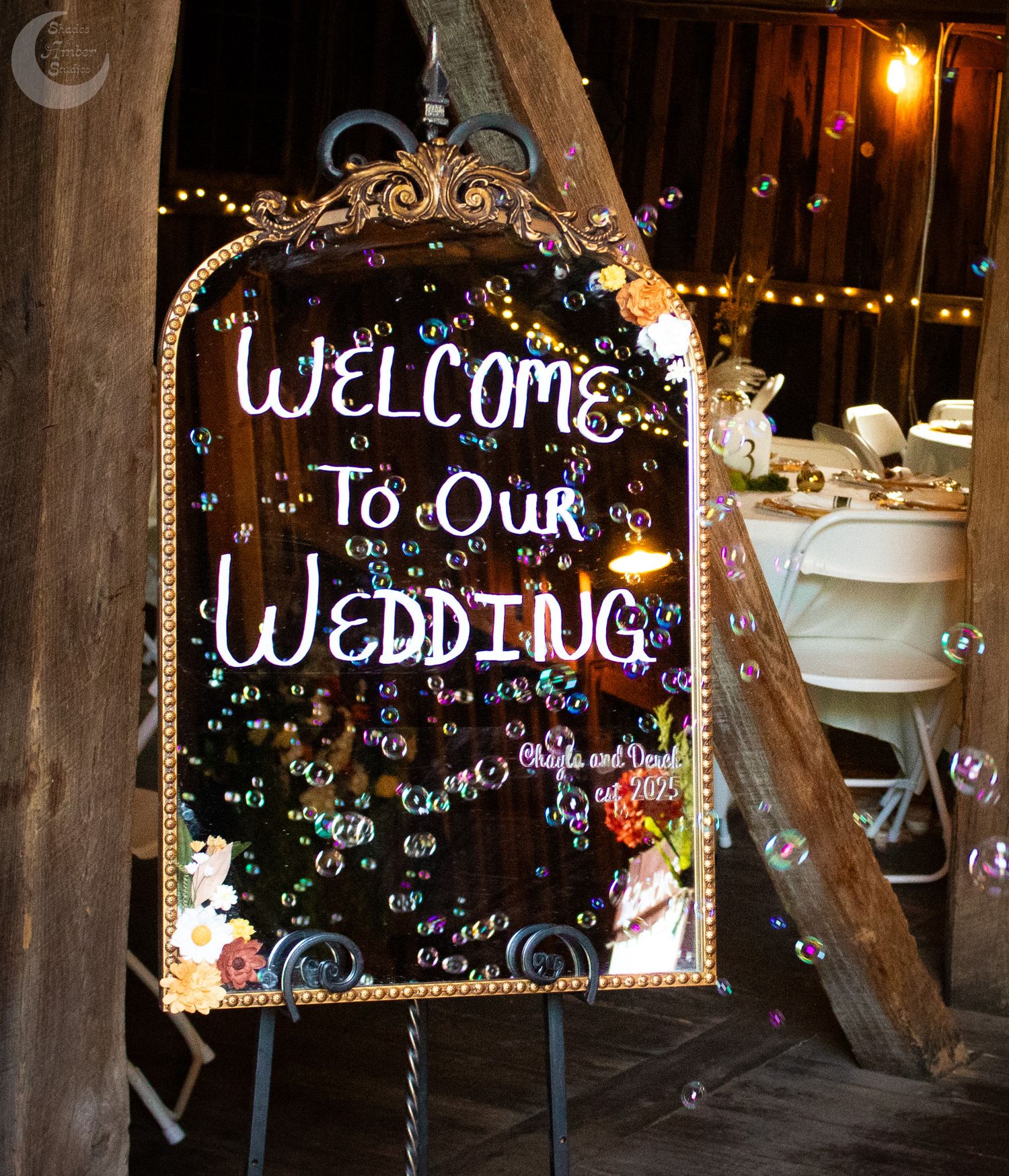 Decorative wedding sign with bubbles floating in the air against a dark rustic wooden backdrop at night.