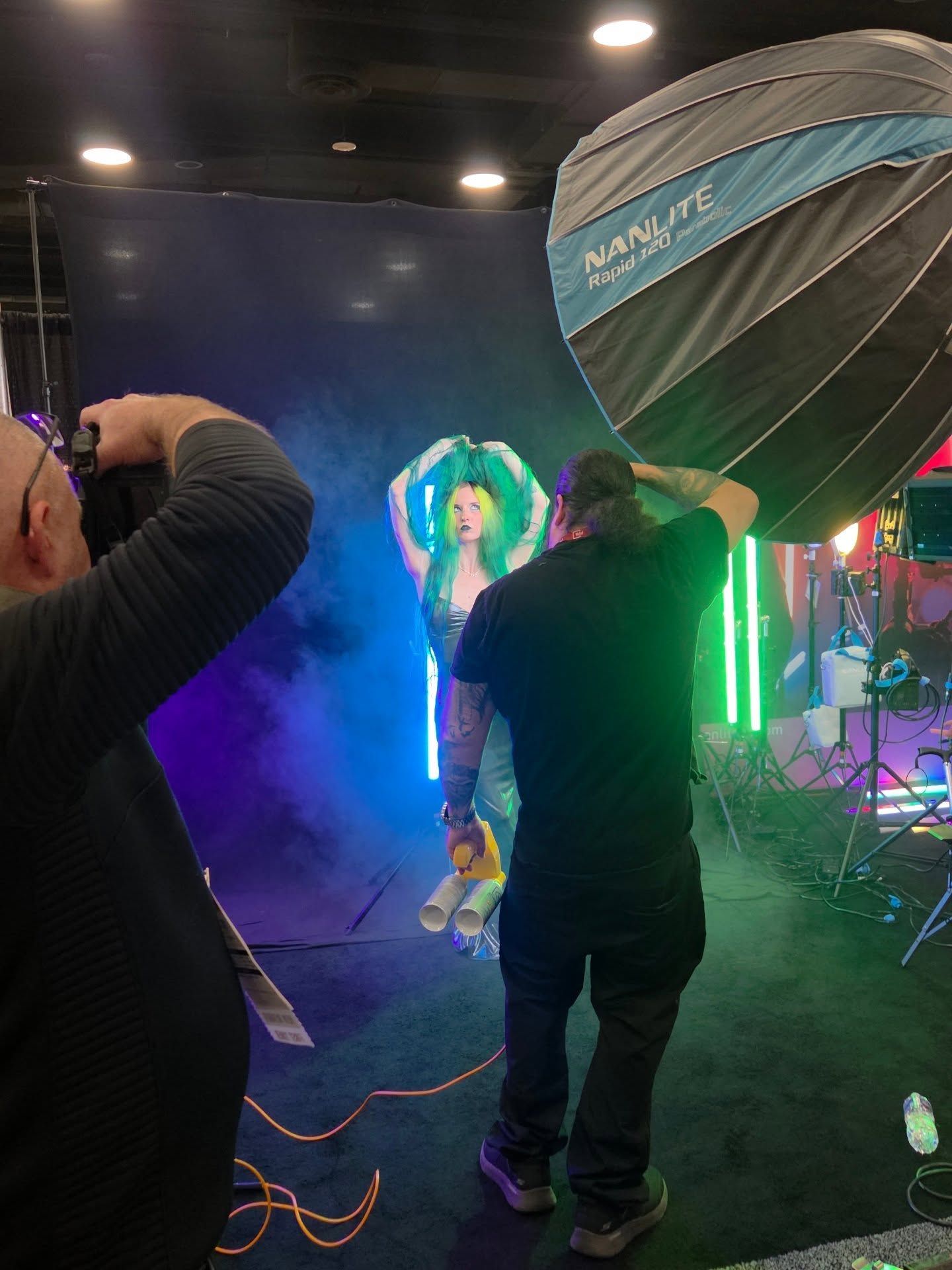 Behind-the-scenes photo shoot setup with lighting equipment and umbrellas in a dark studio.