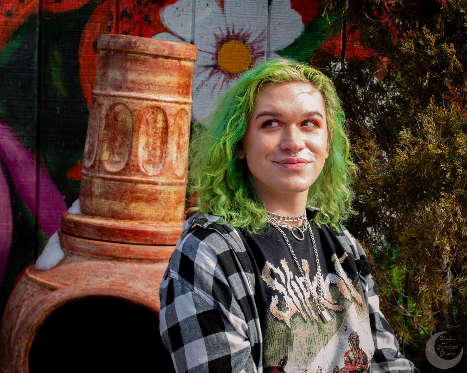 Portrait against colorful mural wall with green hair and plaid flannel shirt.