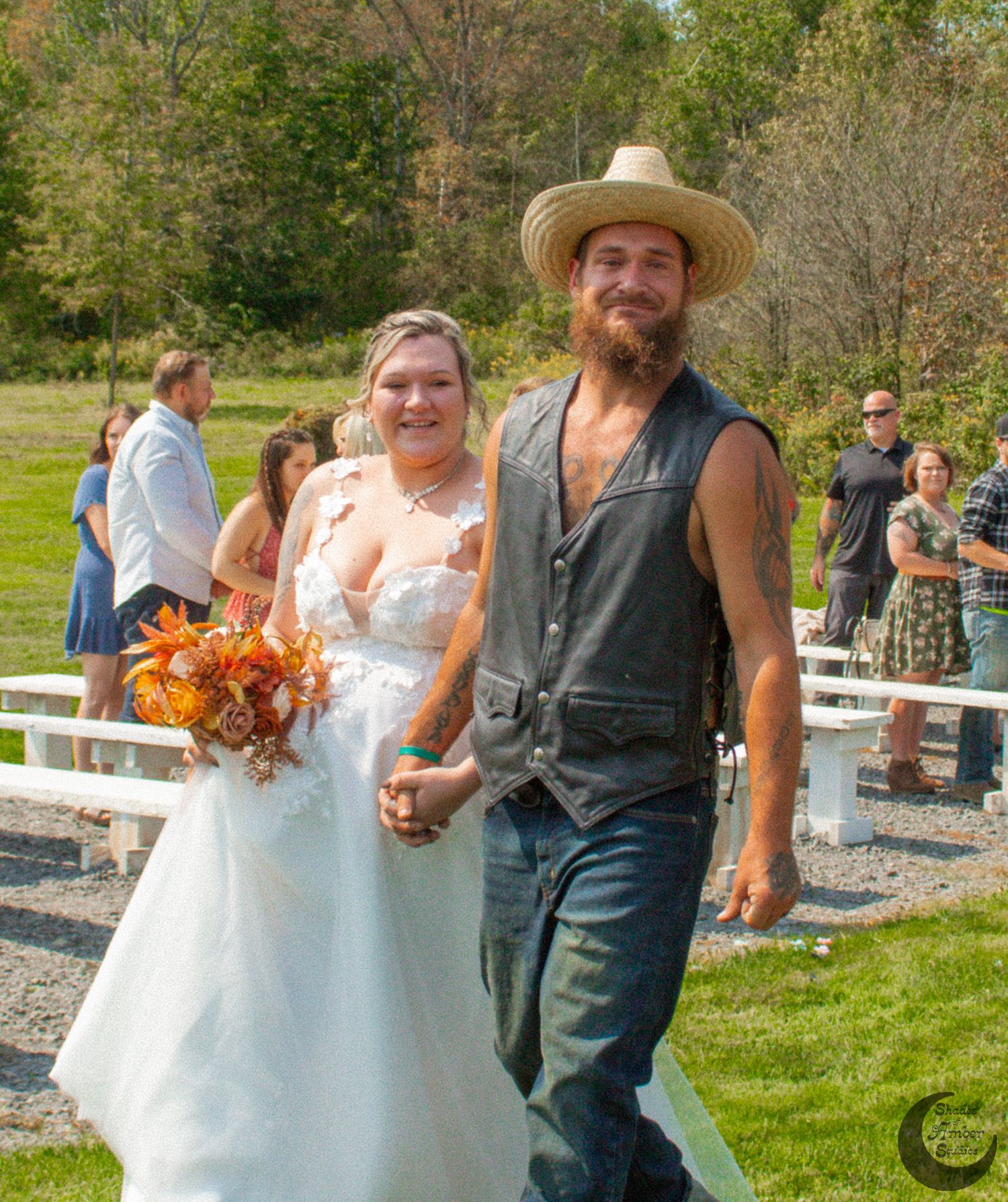 Newlyweds walking together on sunny day with red barn and rolling hills in background.