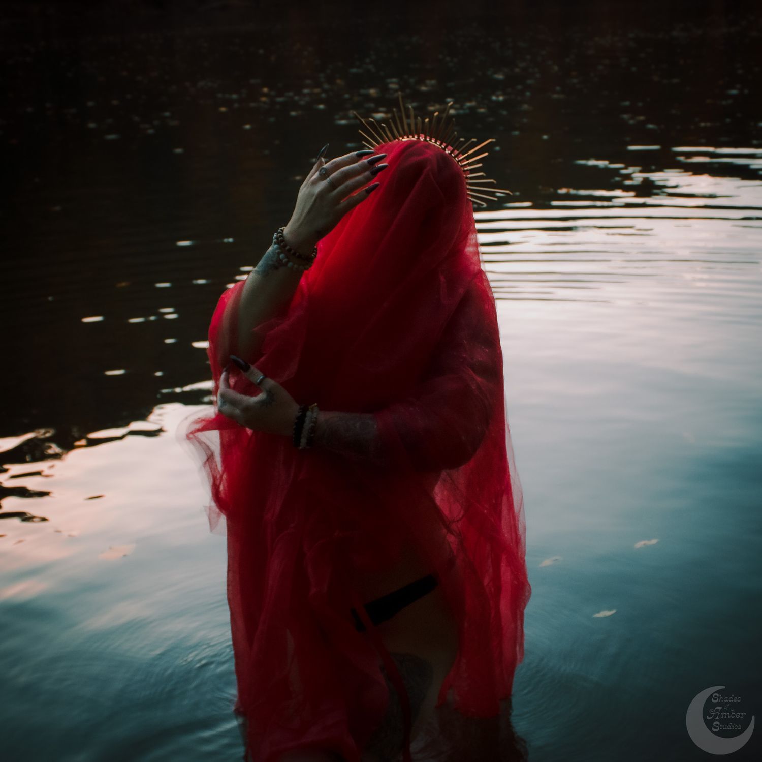 Silhouette covered in billowing red fabric creating dramatic shape against water at dusk.