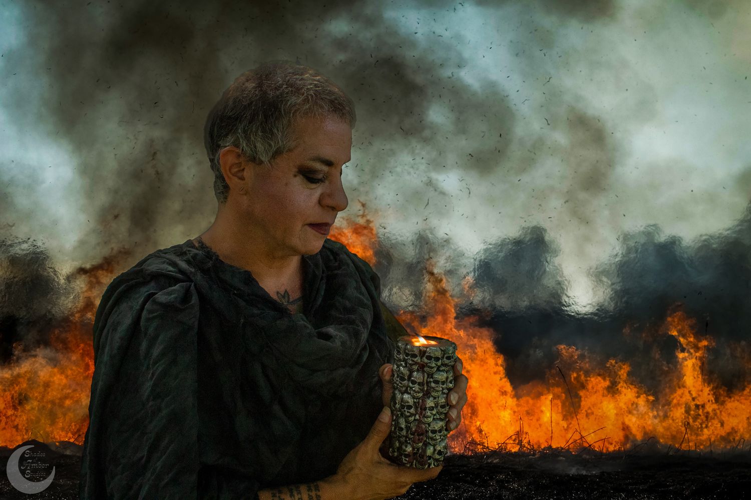 Dramatic portrait against backdrop of flames with figure in black holding a candle.