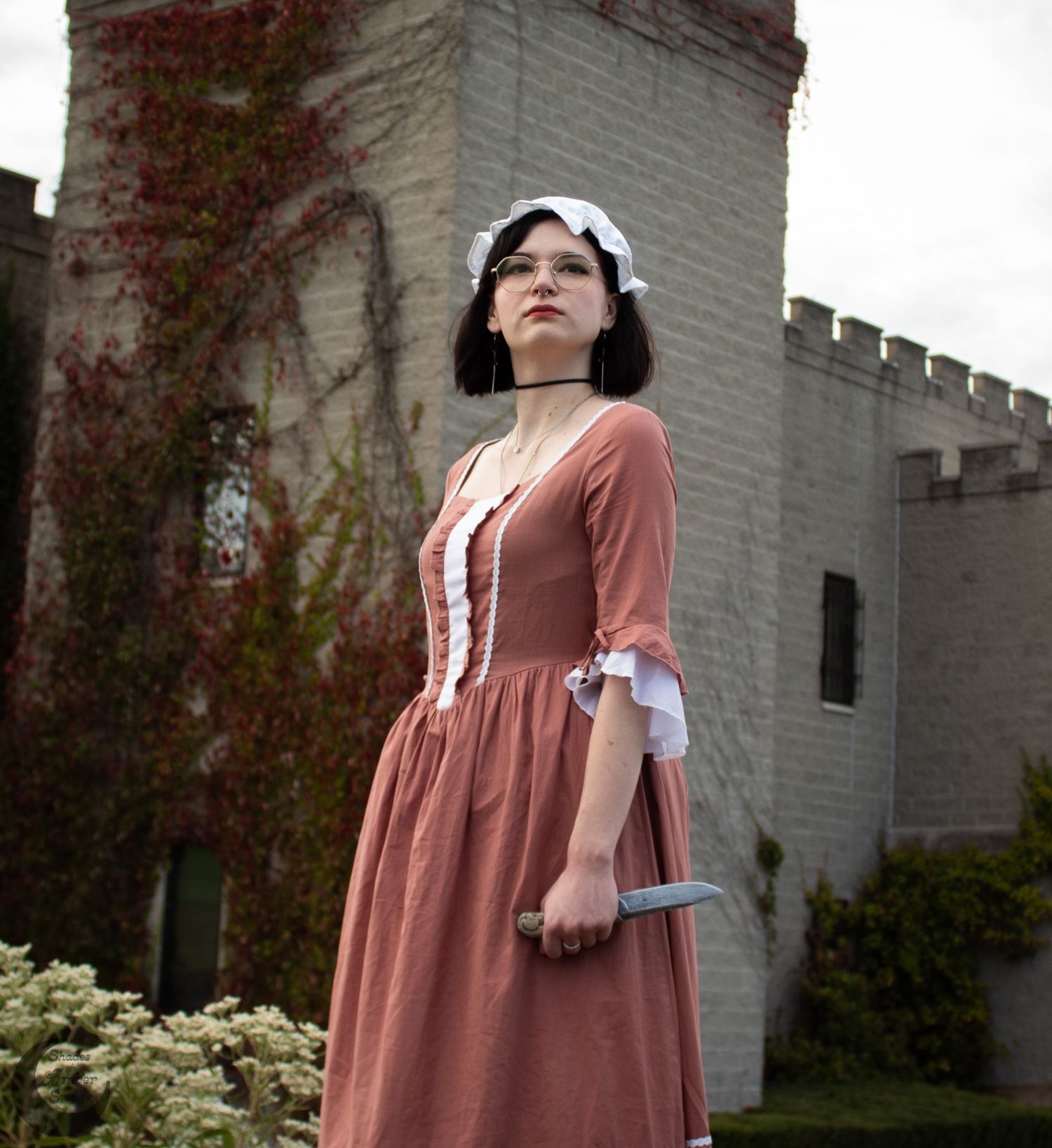Historical dress recreation in salmon pink with white lace trim photographed against stone castle wall.