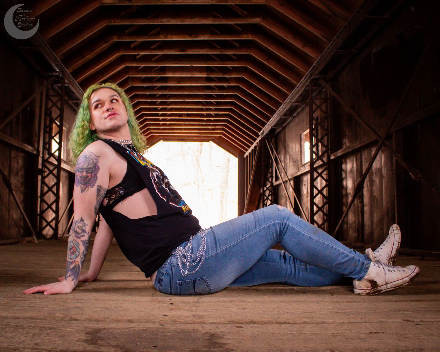 Alternative style figure with green hair poses inside a rustic covered bridge.
