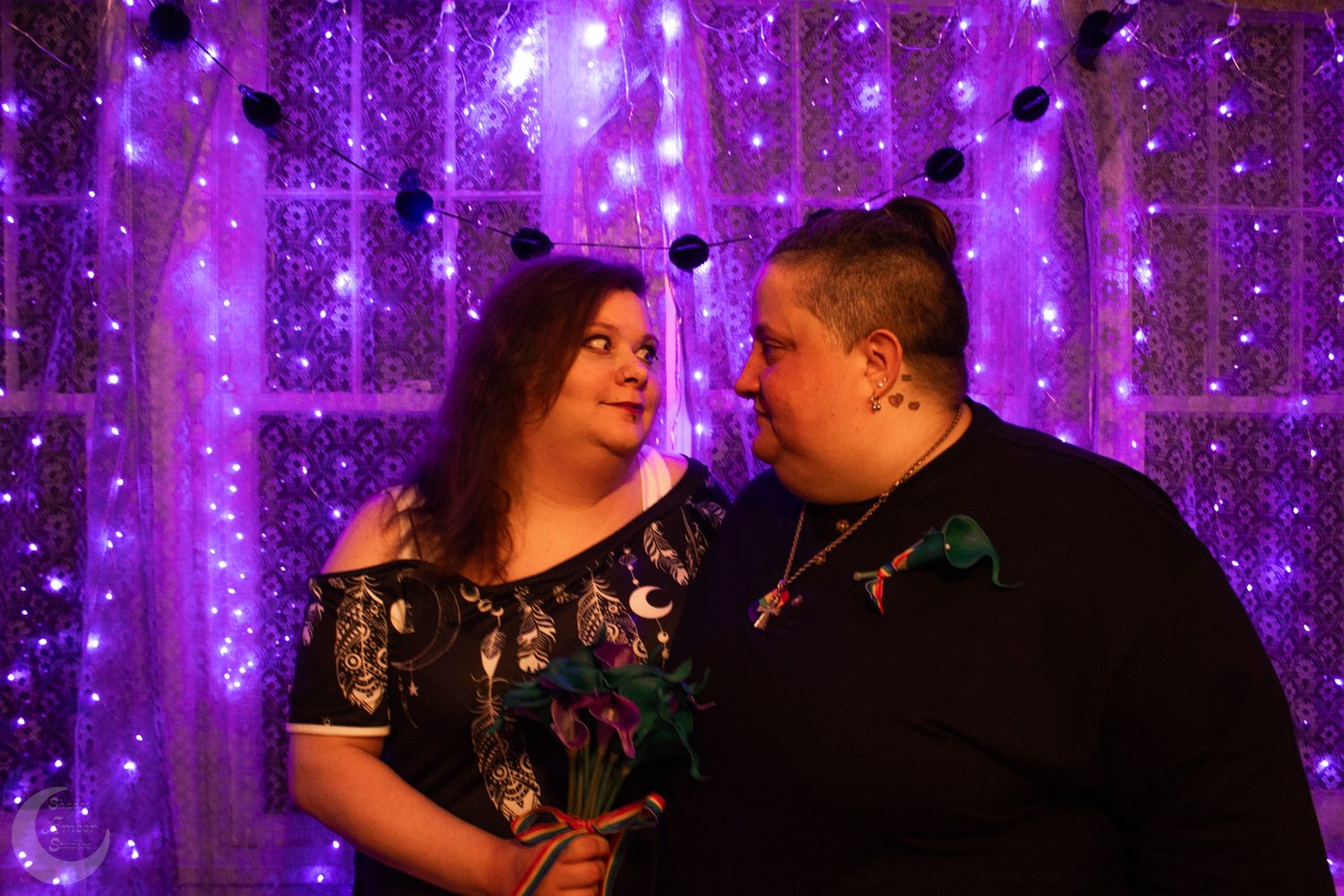 A couple sharing an intimate moment against a backdrop of purple fairy lights at their wedding celebration.