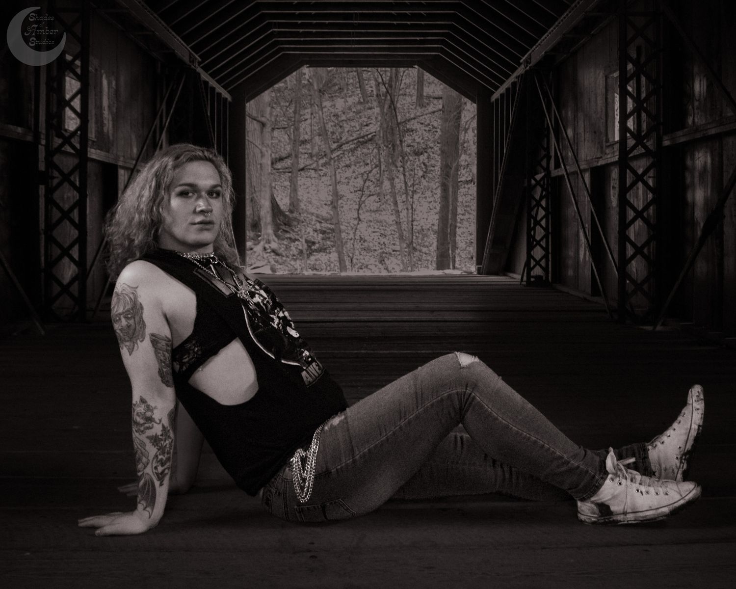 Black and white photo of figure reclining in covered bridge with winter forest view.