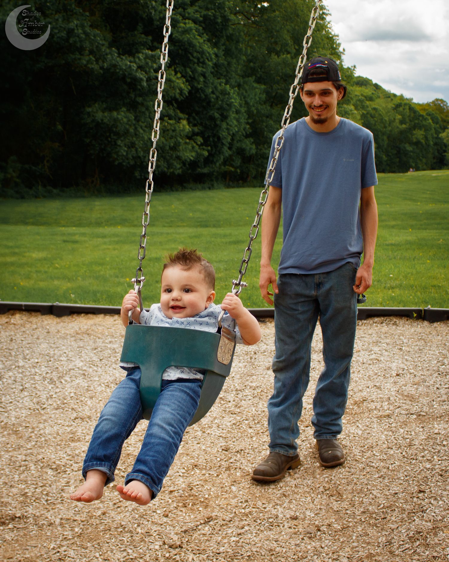 Child enjoying a swing at a playground with adults standing nearby on a sunny day.