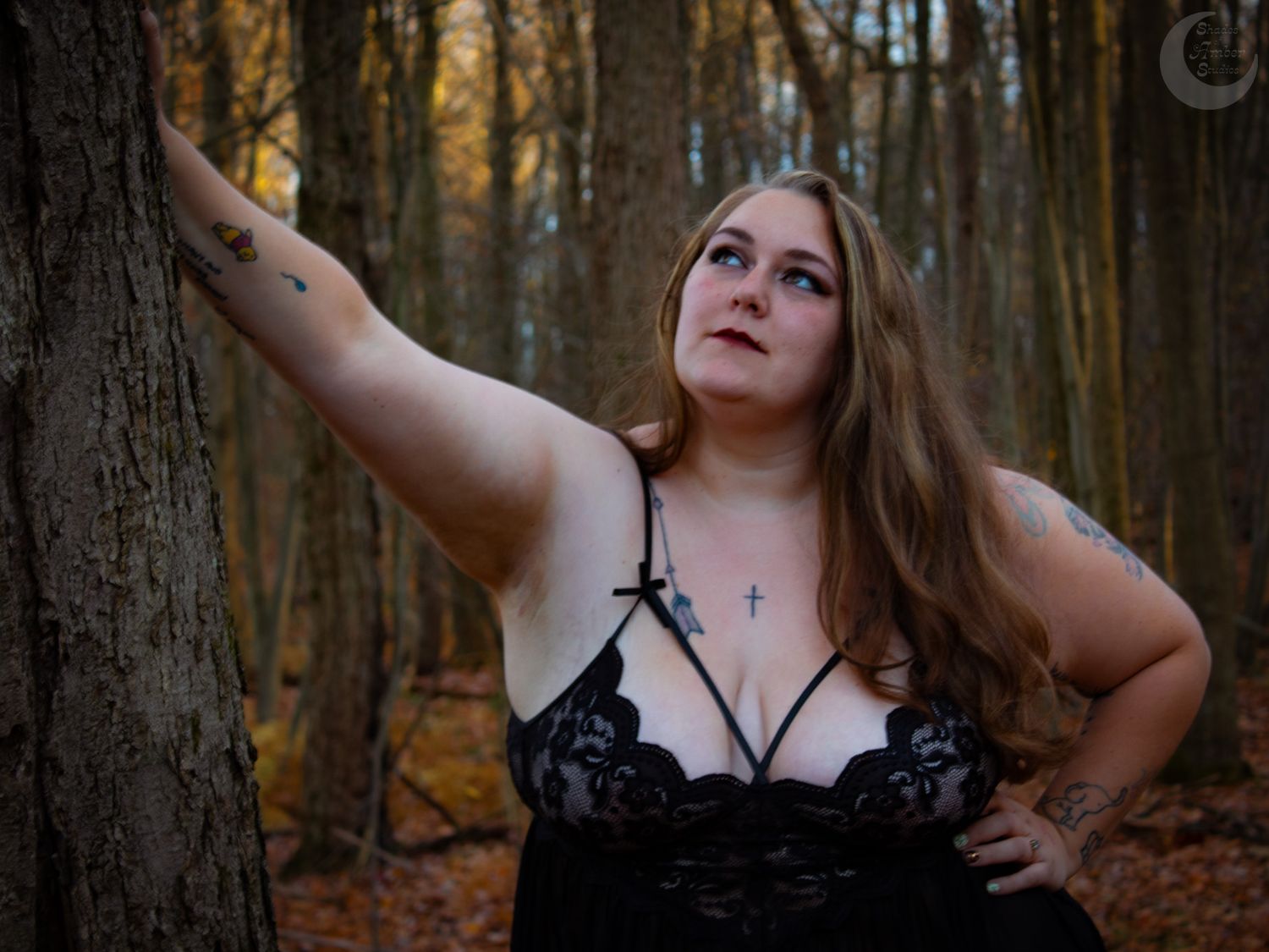 An artistic boudoir photo shoot in an autumn forest with a model posing against a tree trunk.