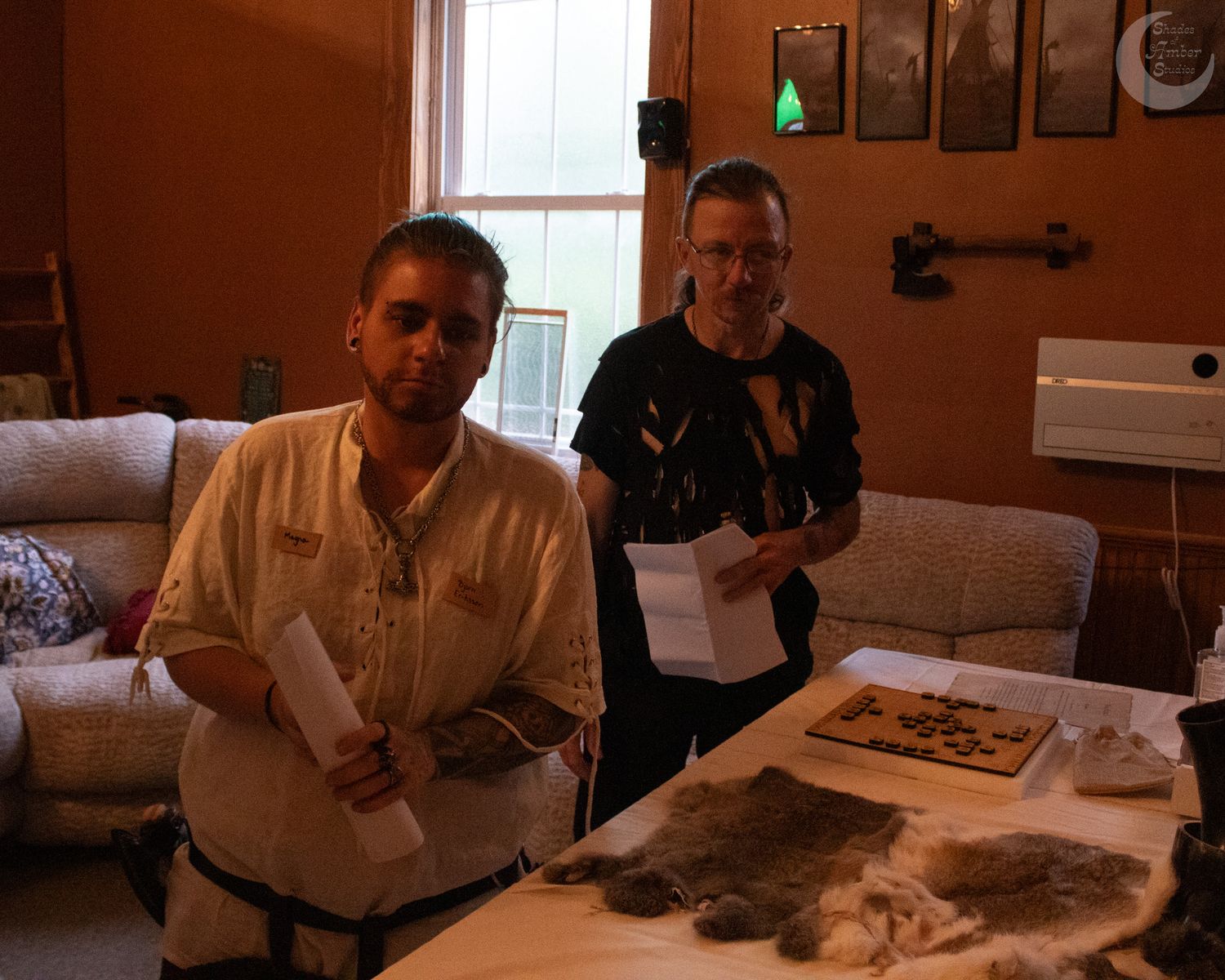 Two people sit at a table examining papers and materials in a cozy home interior setting.