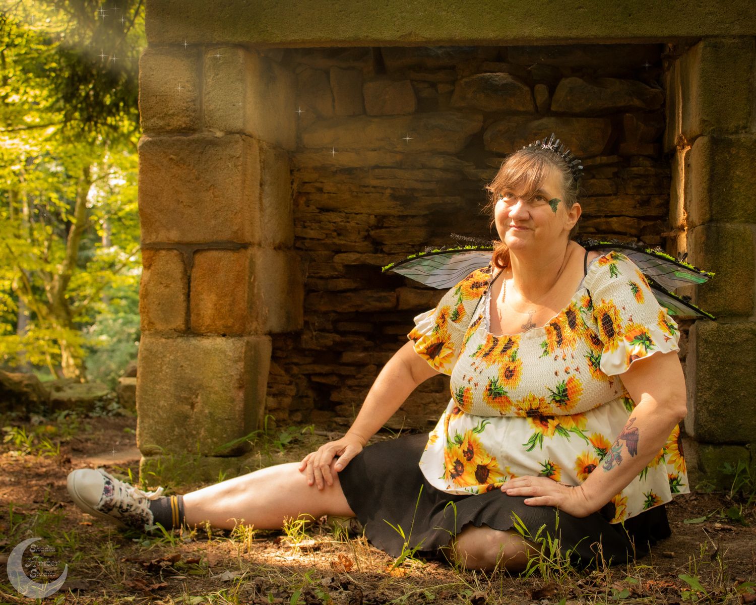 A person in a floral dress sits under a stone archway during a sunny outdoor photo session.