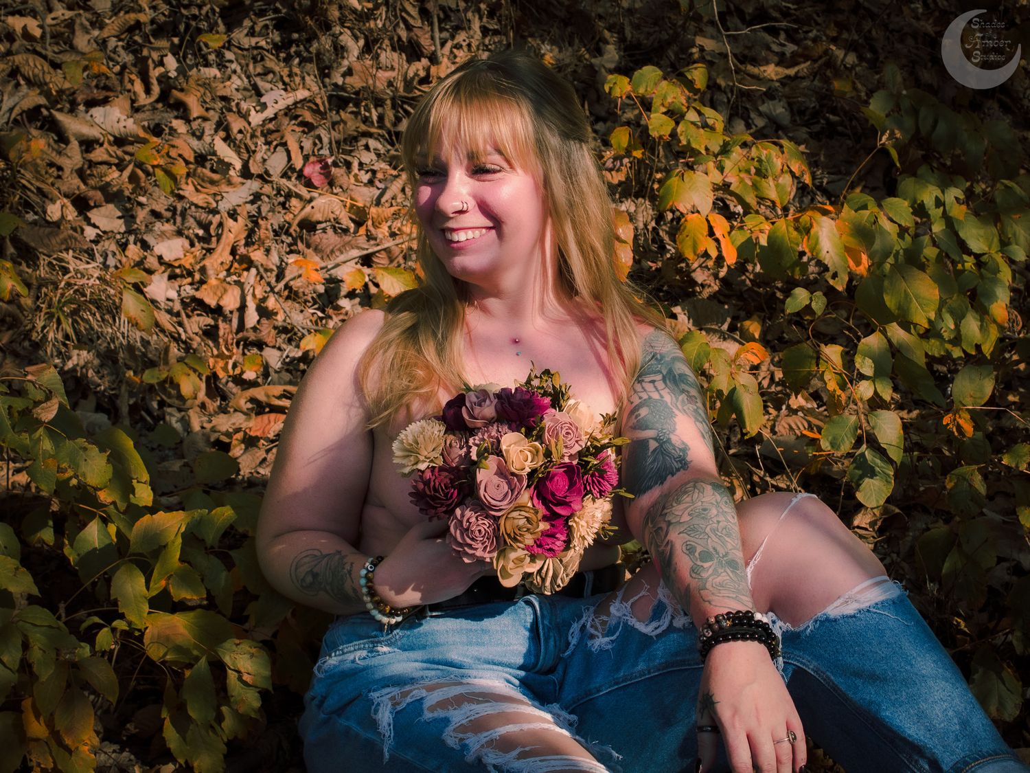 A woman in a blue dress sits among autumn grapevines holding a glass of red wine at sunset.
