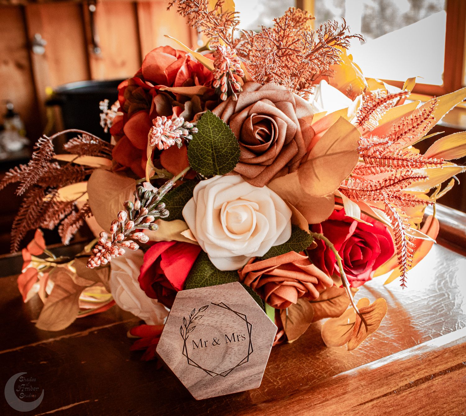Rustic autumn wedding bouquet with orange and pink roses and a wooden hexagonal name tag.