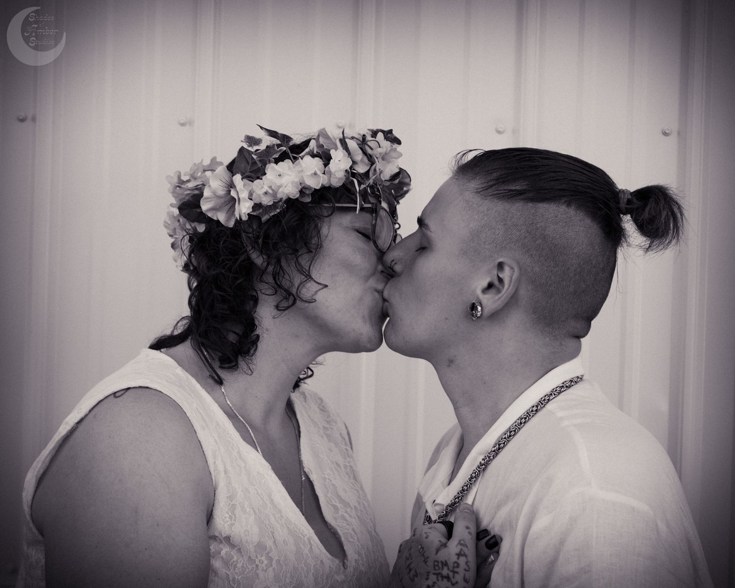 A romantic black and white photograph showing a tender kiss, with one person wearing a floral crown and white dress.