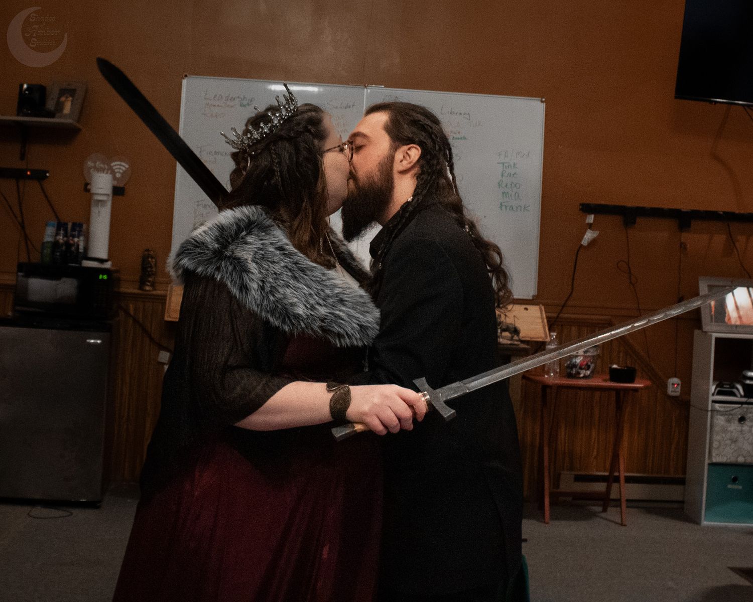 A romantic ceremonial kiss between a couple in medieval-inspired gothic attire.