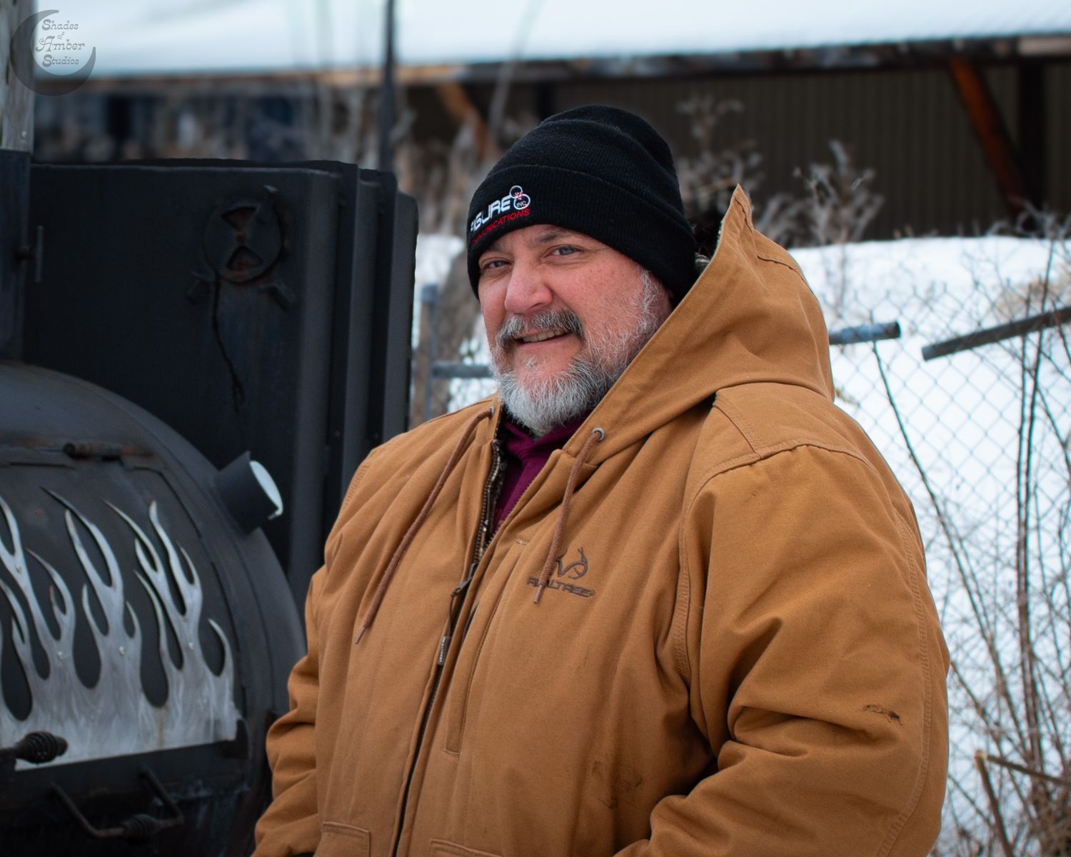 A person wearing a brown Carhartt jacket and beanie smiles outdoors in winter.