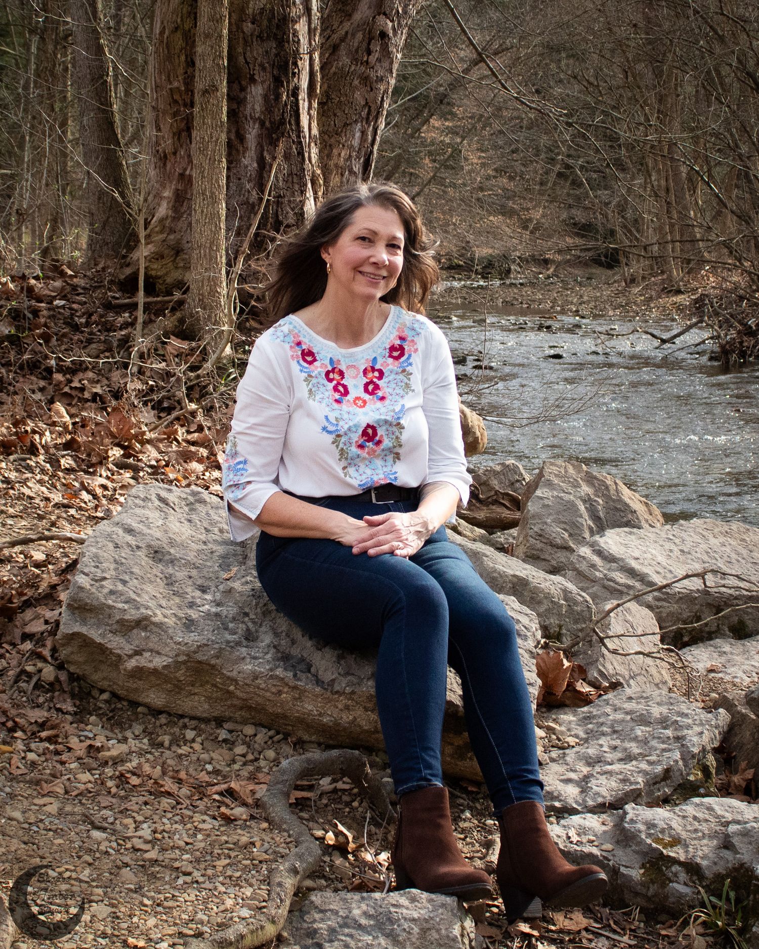 Natural outdoor portrait of someone sitting on rocks by a flowing stream wearing embroidered top.