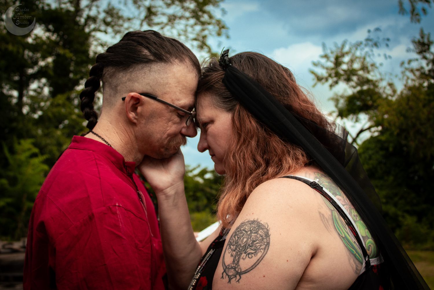 Romantic couple embraces intimately outdoors against a lush green forest background.