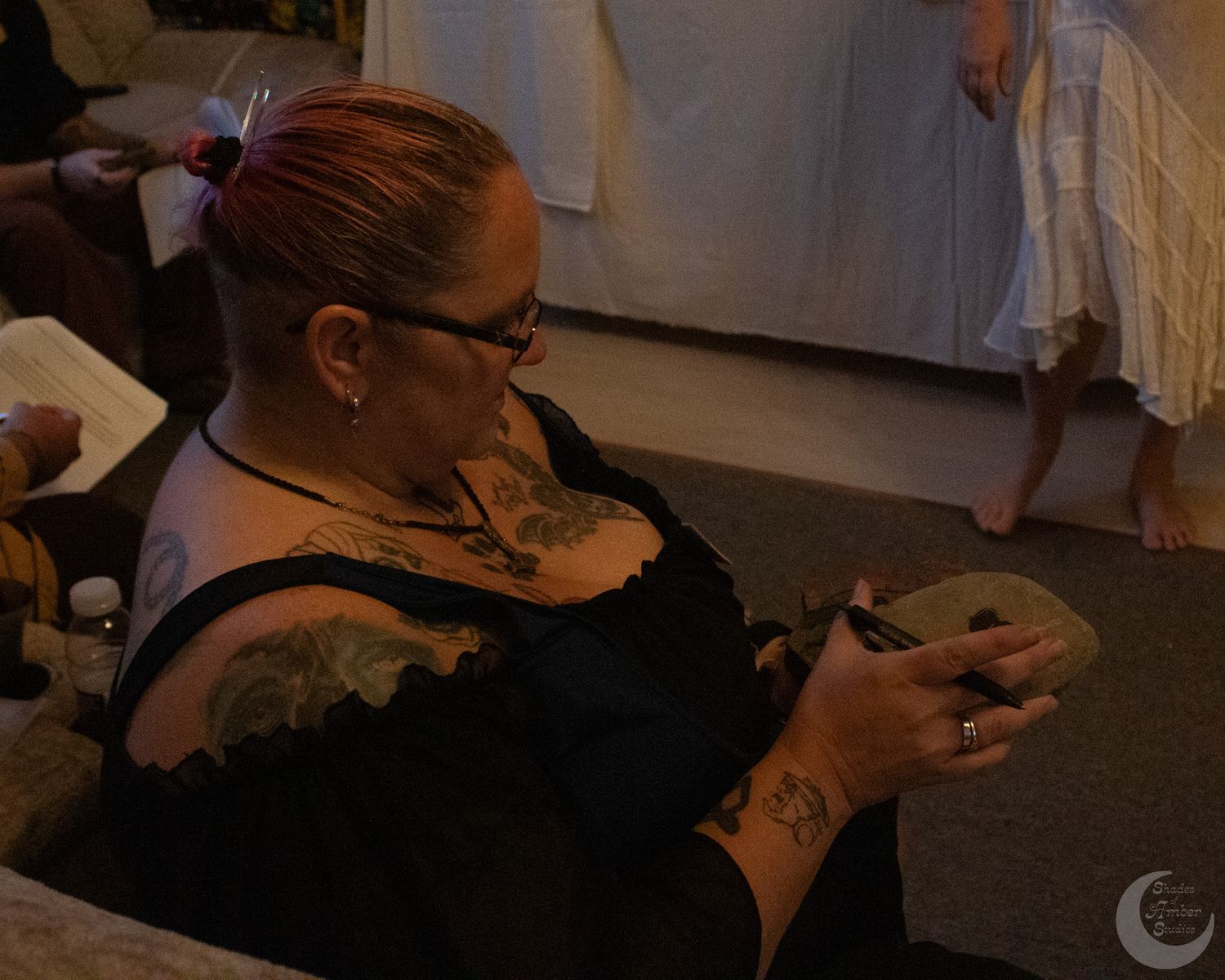 Someone in a black top with tattoos looks at a handheld device while sitting down.