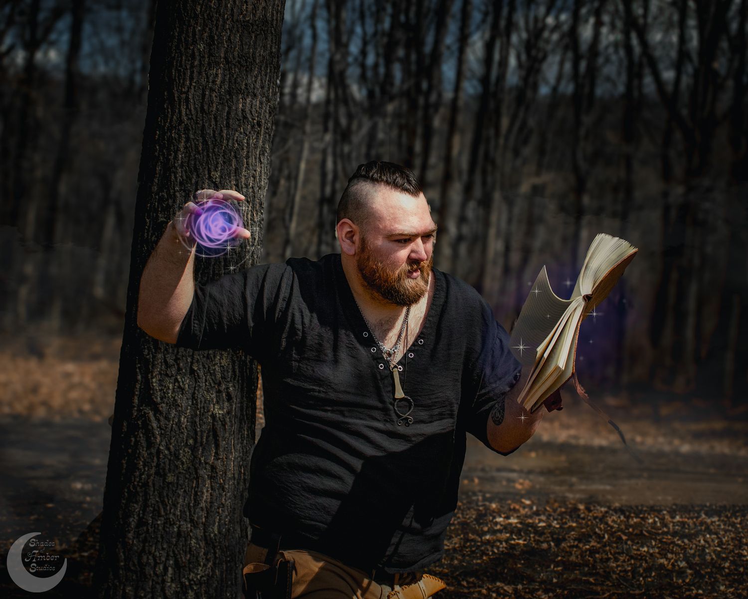 Bearded person in dark clothing holds mystical glowing orb and book while leaning against tree in moody forest setting.