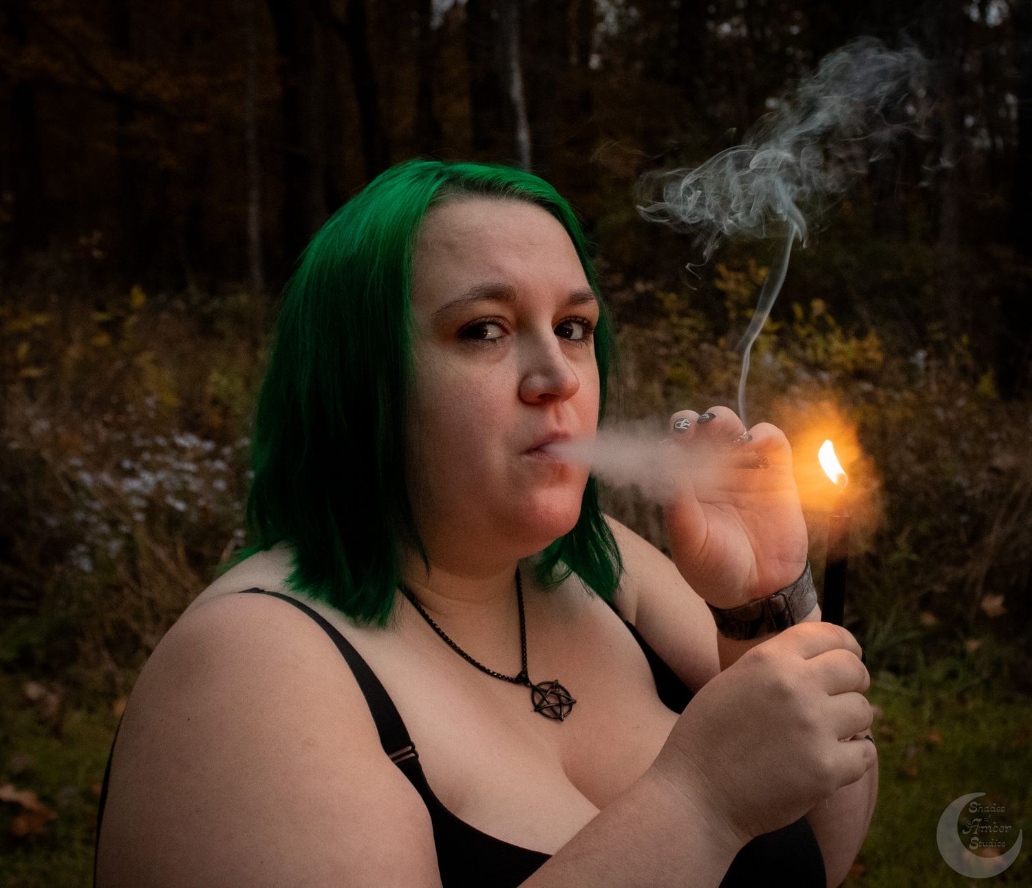 Person with green hair lighting something with smoke in autumn forest setting.