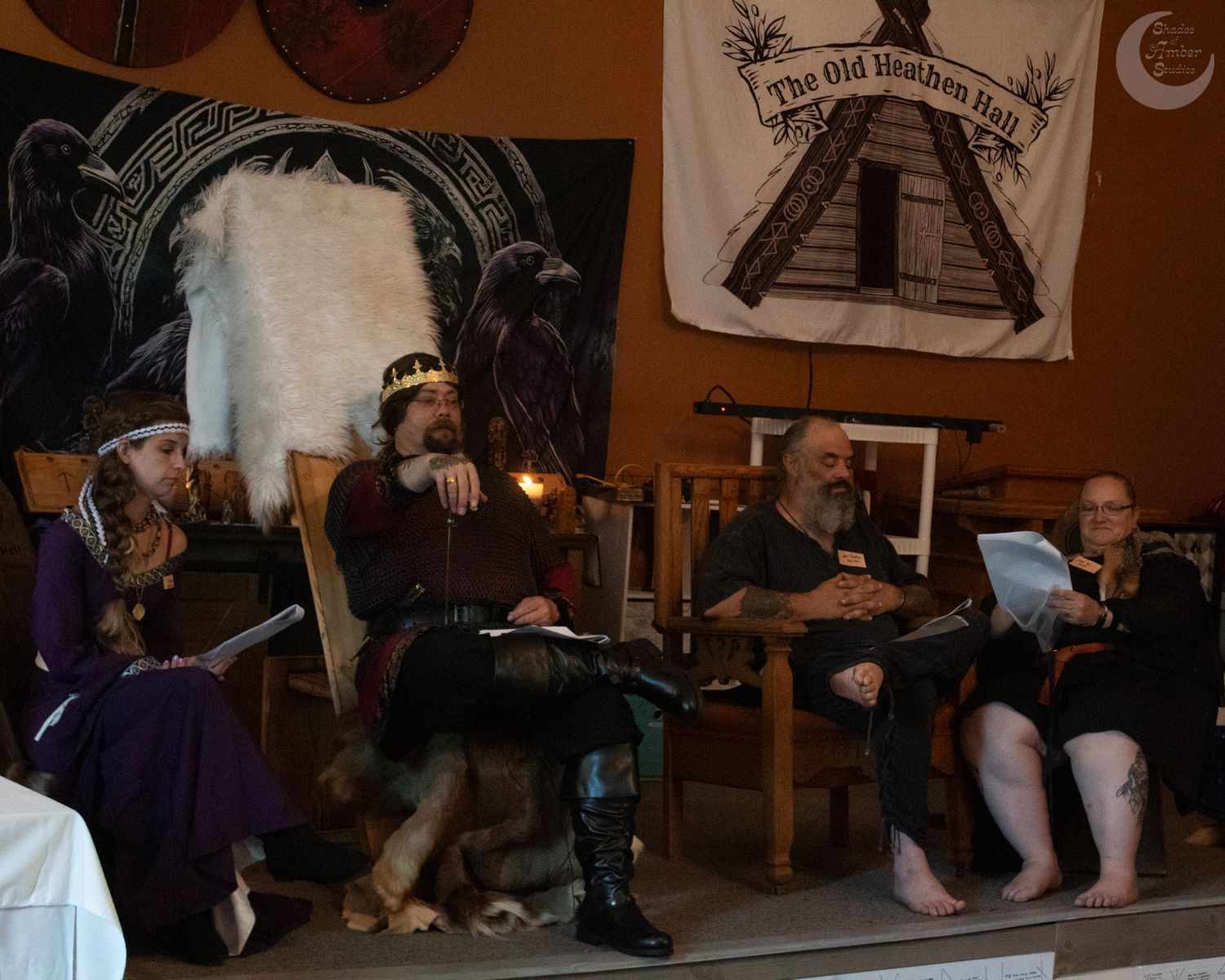 People gathered in a dimly lit room with medieval-themed decorations and a pyramid artwork on the wall in the background.